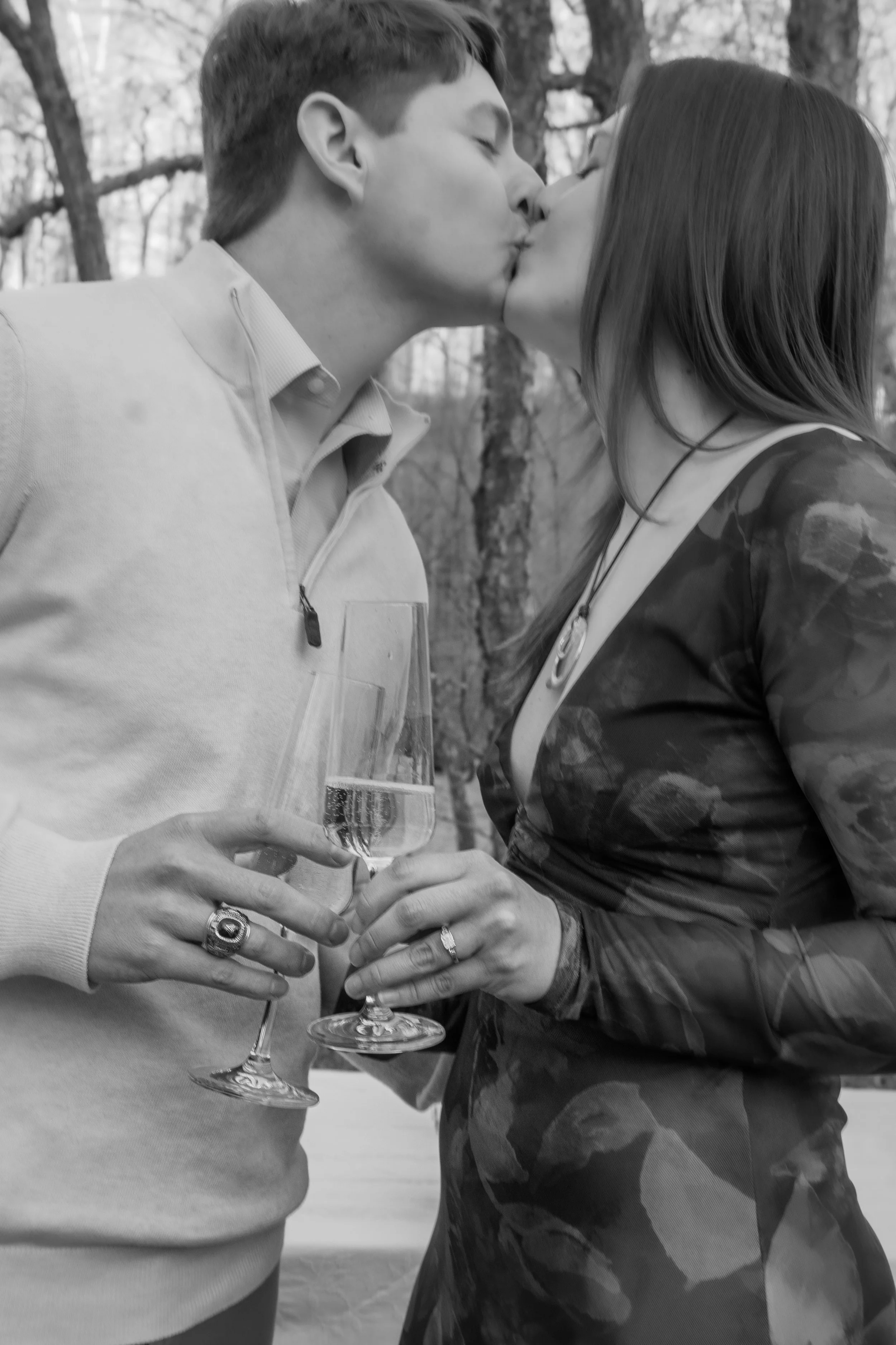 Engagement Photography by Will Locke near Richmond, VA in Montpelier. A man and woman kissing while holding champagne glasses outdoors during sunset, with a table of flowers nearby.