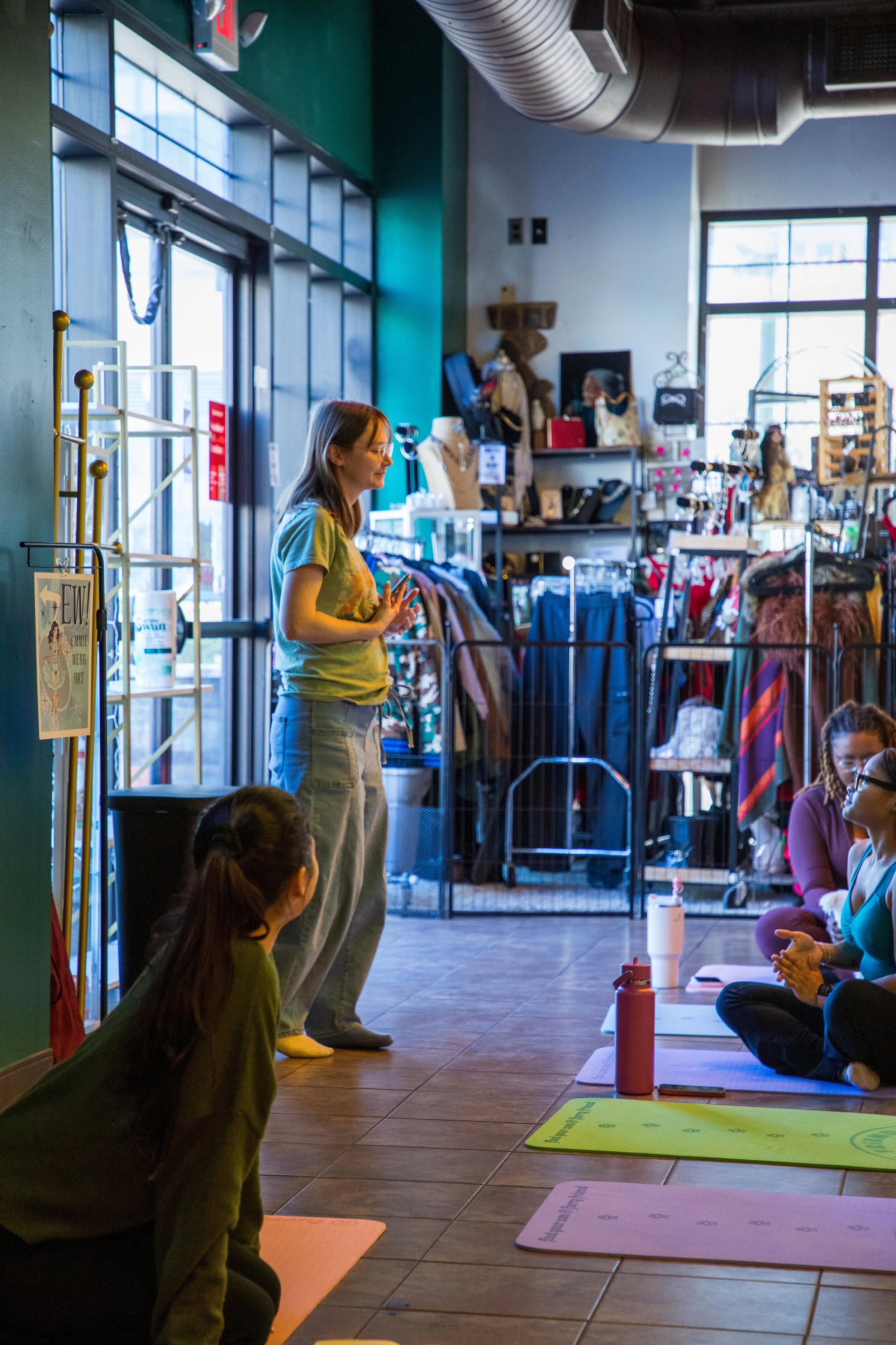 Marketing and Event Photography by Will Locke. A woman standing and speaking to a seated group in a yoga class in a retail store with clothing and accessories in the background.