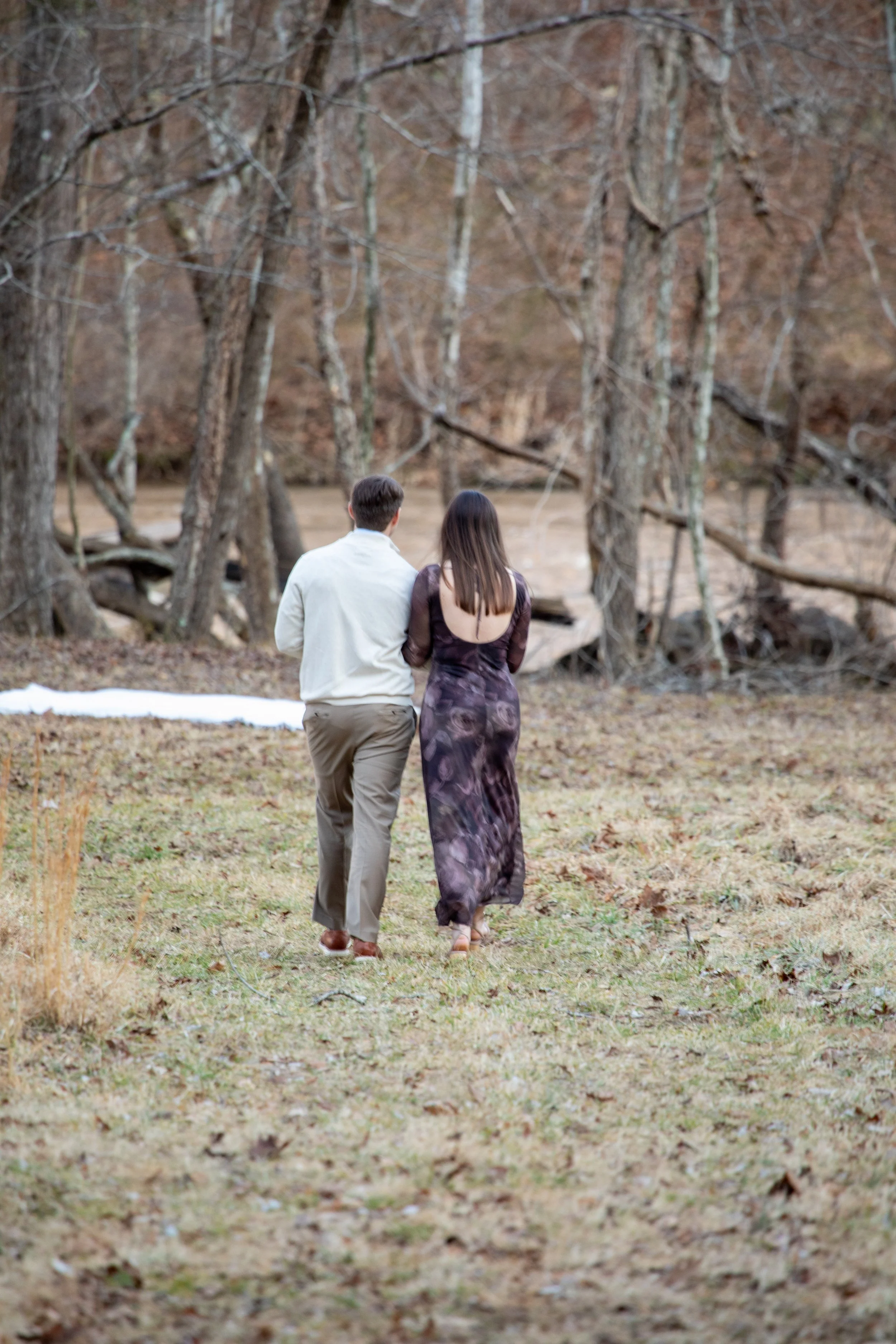Engagement Photography by Will Locke near Richmond, VA in Montpelier. A couple walks to a white cloth on the ground near a wooded area with a stream on a fall day, with a table on the left side with white tablecloth.