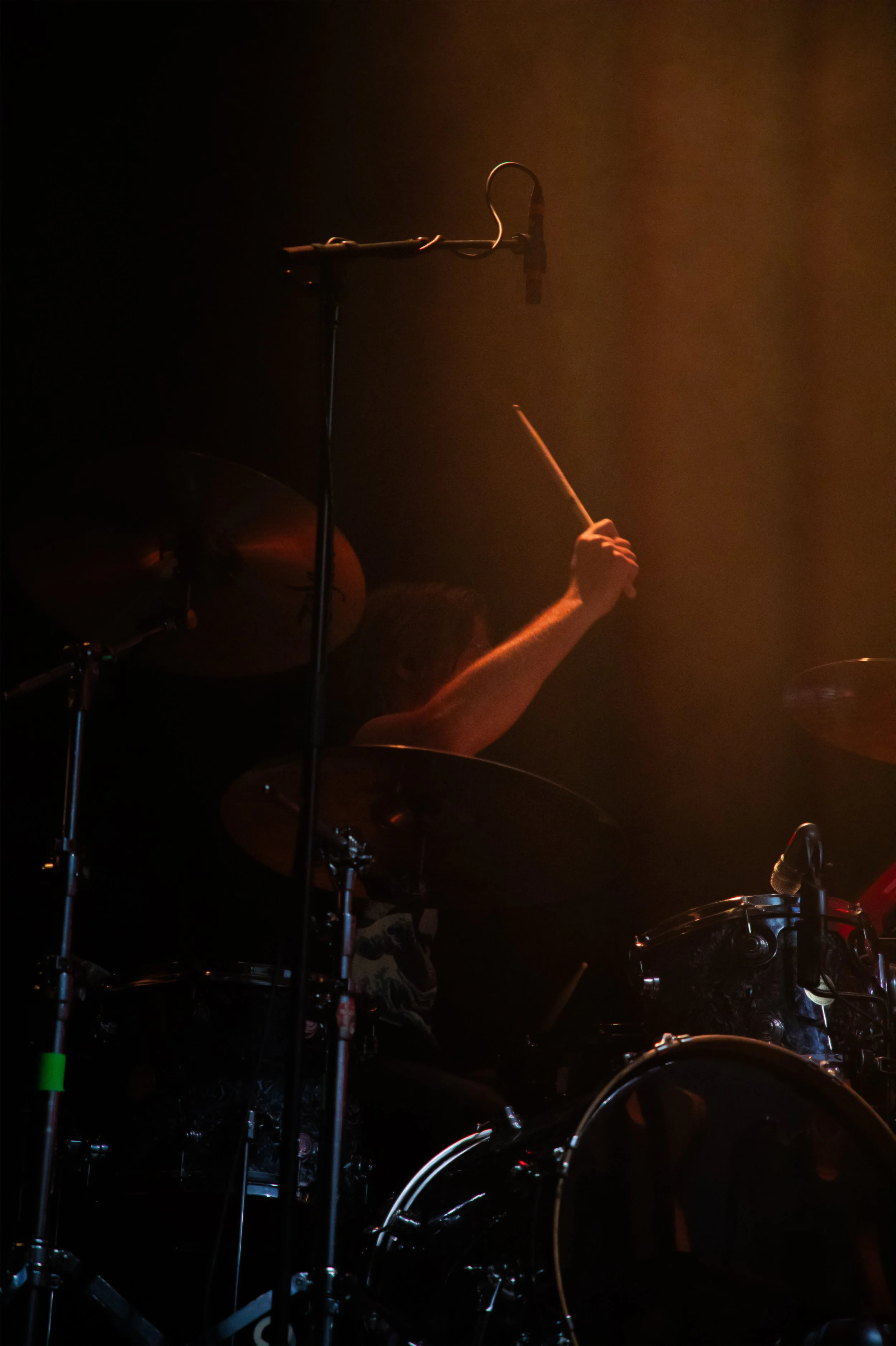 Concert Photography by Will Locke. A drummer playing on stage with dark background, illuminated by warm orange lights.