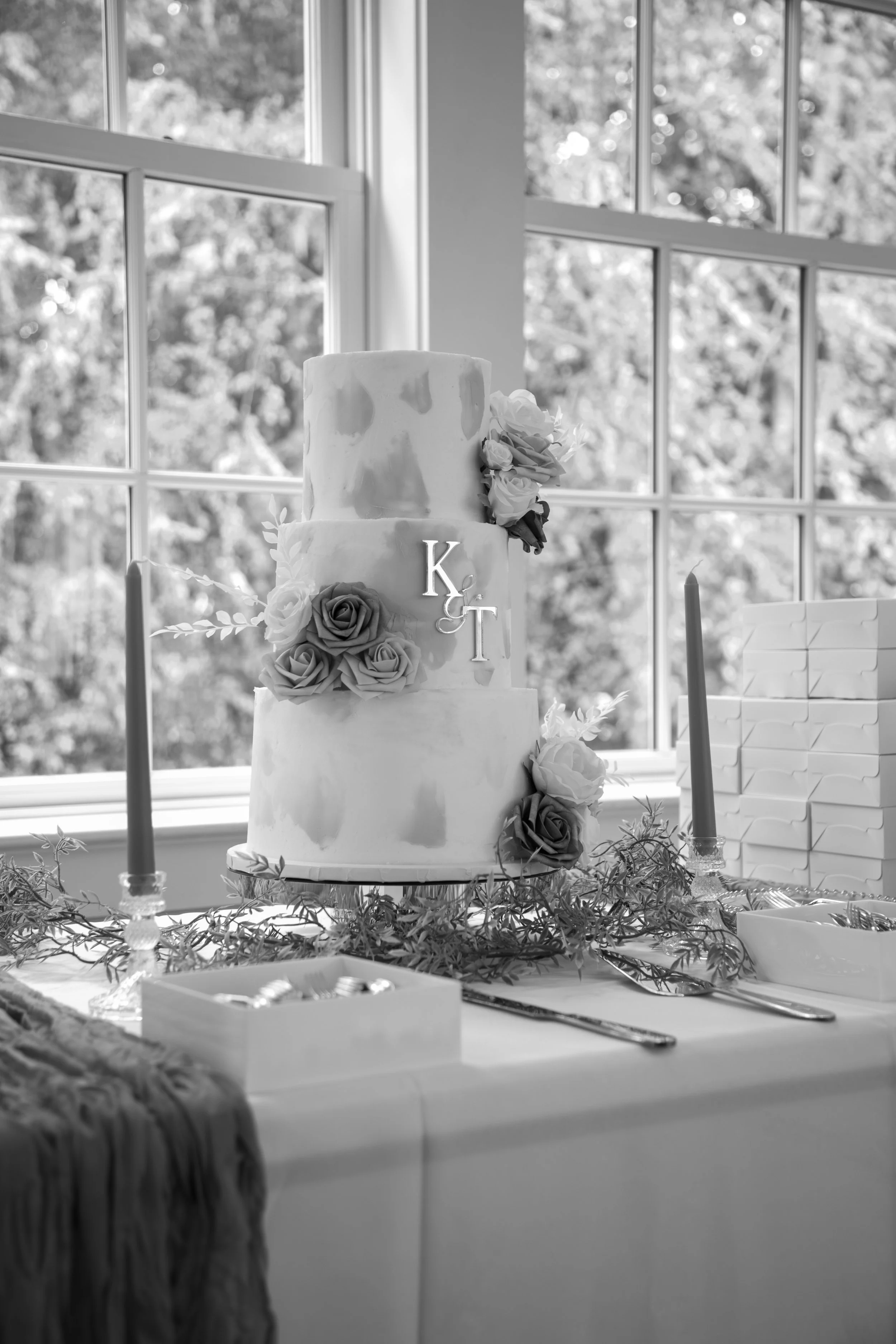 Wedding Photography by Will Locke. A three-tiered wedding cake with floral decorations and monogram initials, set on a decorated table near a window.