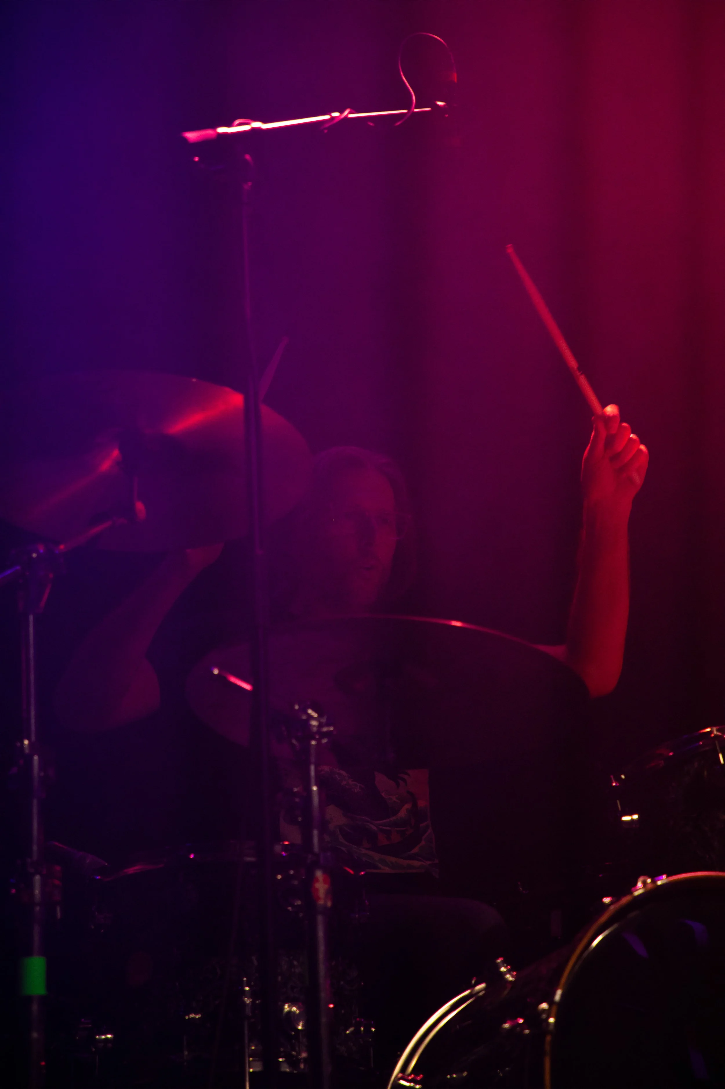 Concert Photography by Will Locke. A musician playing drums on a stage illuminated by pink and purple lights.