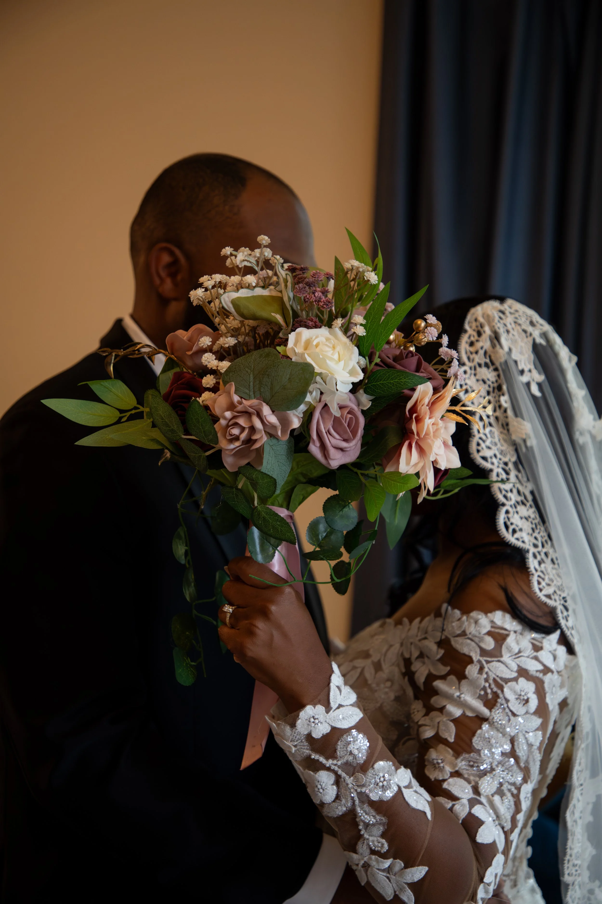Wedding Photography by Will Locke. A bride and groom sharing a moment with the bride holding a bouquet of flowers, her face partially covered by the bouquet, and the groom's face slightly visible.