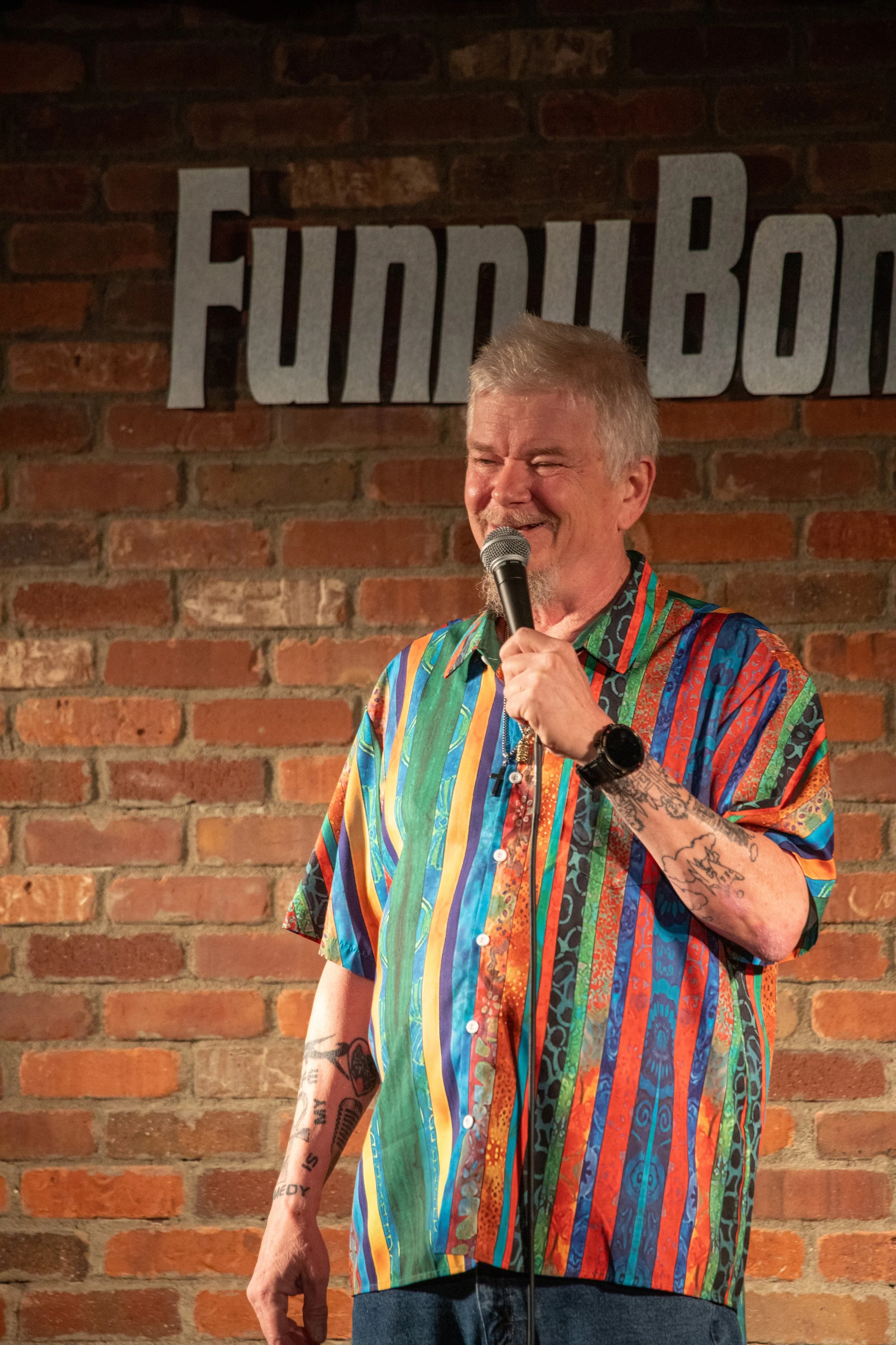 Comedy Photography by Will Locke in Norfolk, VA. A older man performs on stage while smiling in between jokes.