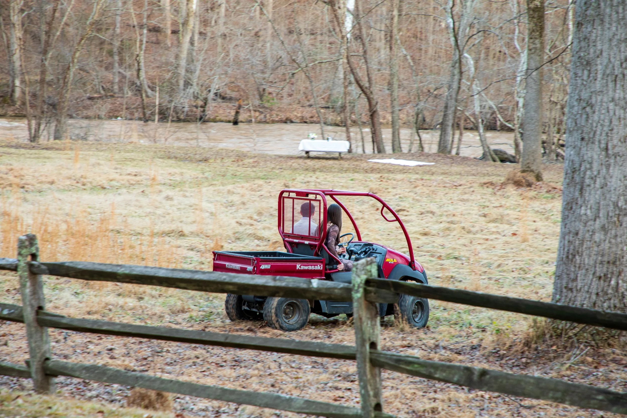 Engagement Photography by Will Locke near Richmond, VA in Montpelier. A newly engaged couple riding a red Kawasaki Mule utility vehicle through a park or wooded area during fall or early winter.
