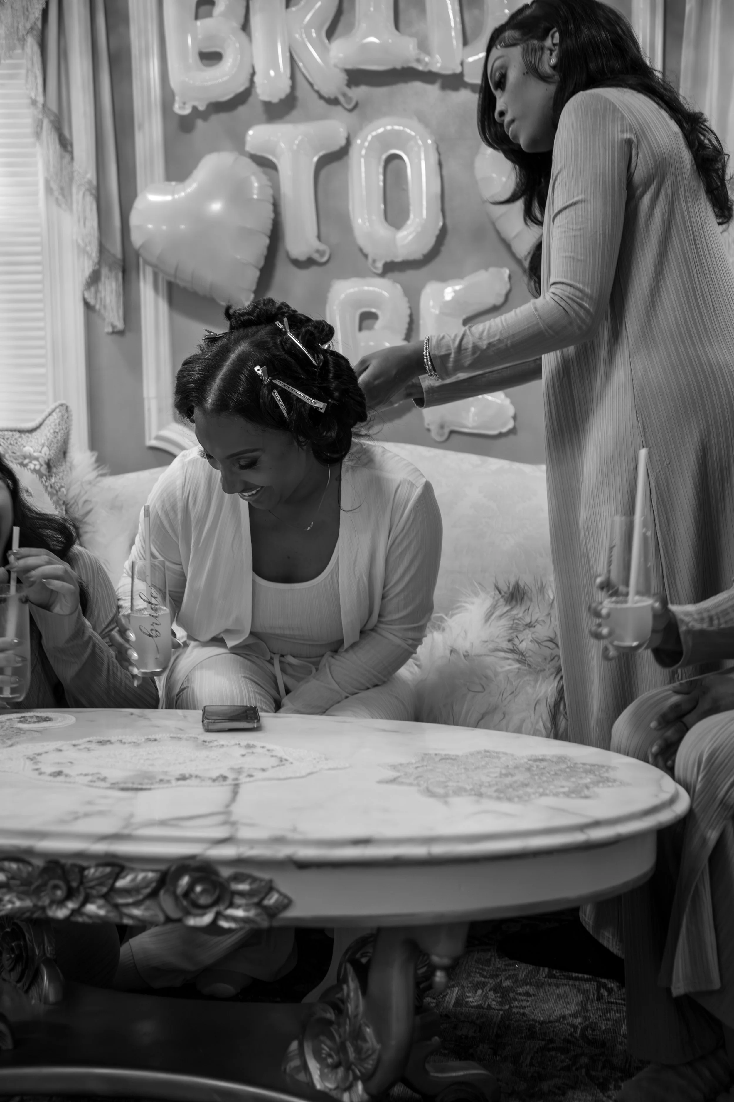 Wedding Photography by Will Locke. Women celebrating a bridal shower with cake and drinks, with balloons and a 'Bride To Be' sign in the background.