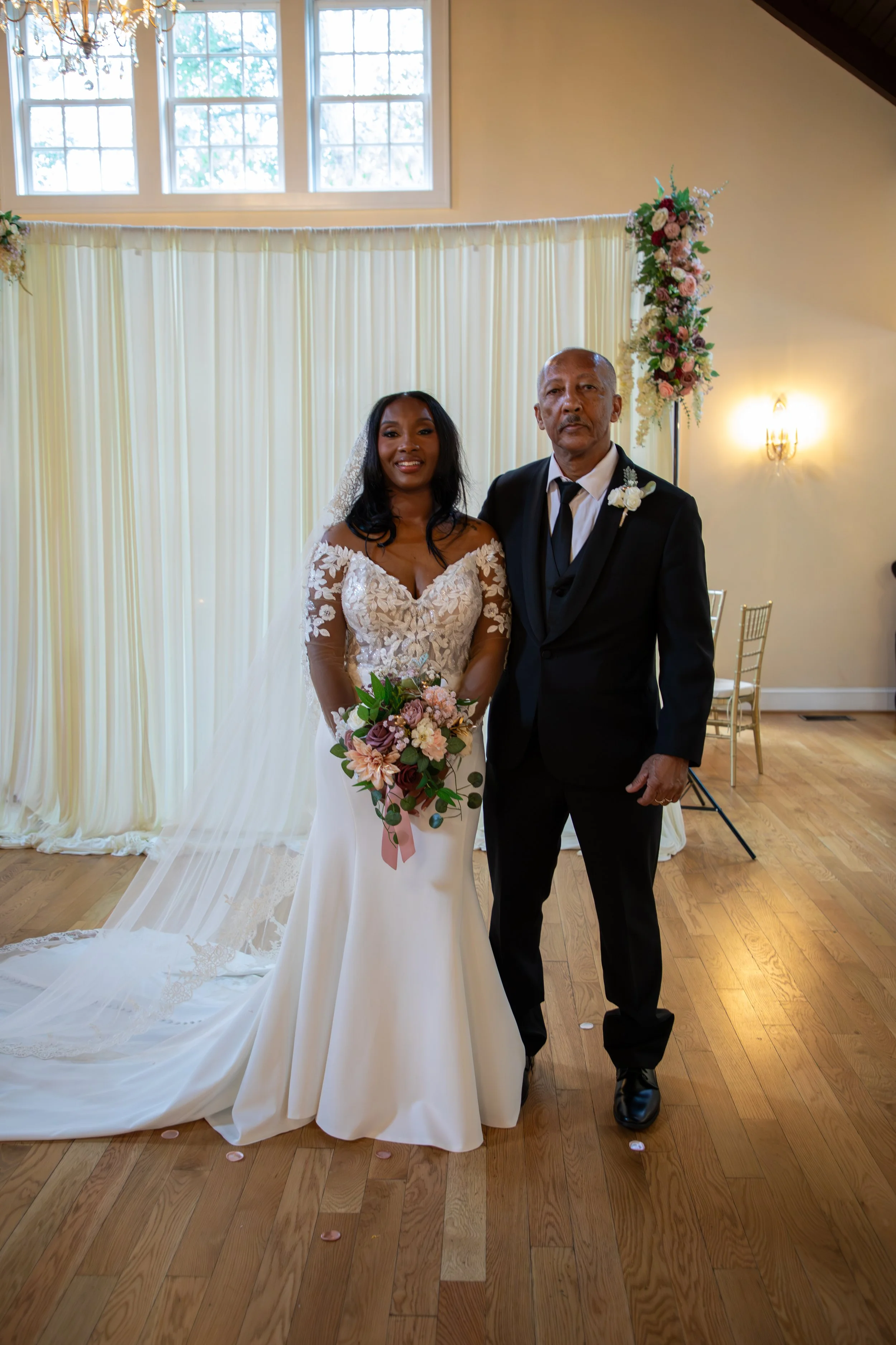 Photo & Video by Will Locke Wedding Photography at the Woman's Club of Portsmouth in Virginia. A bride in a lace-embellished wedding gown holding a bouquet standing next to an older man in a black suit at a wedding ceremony.