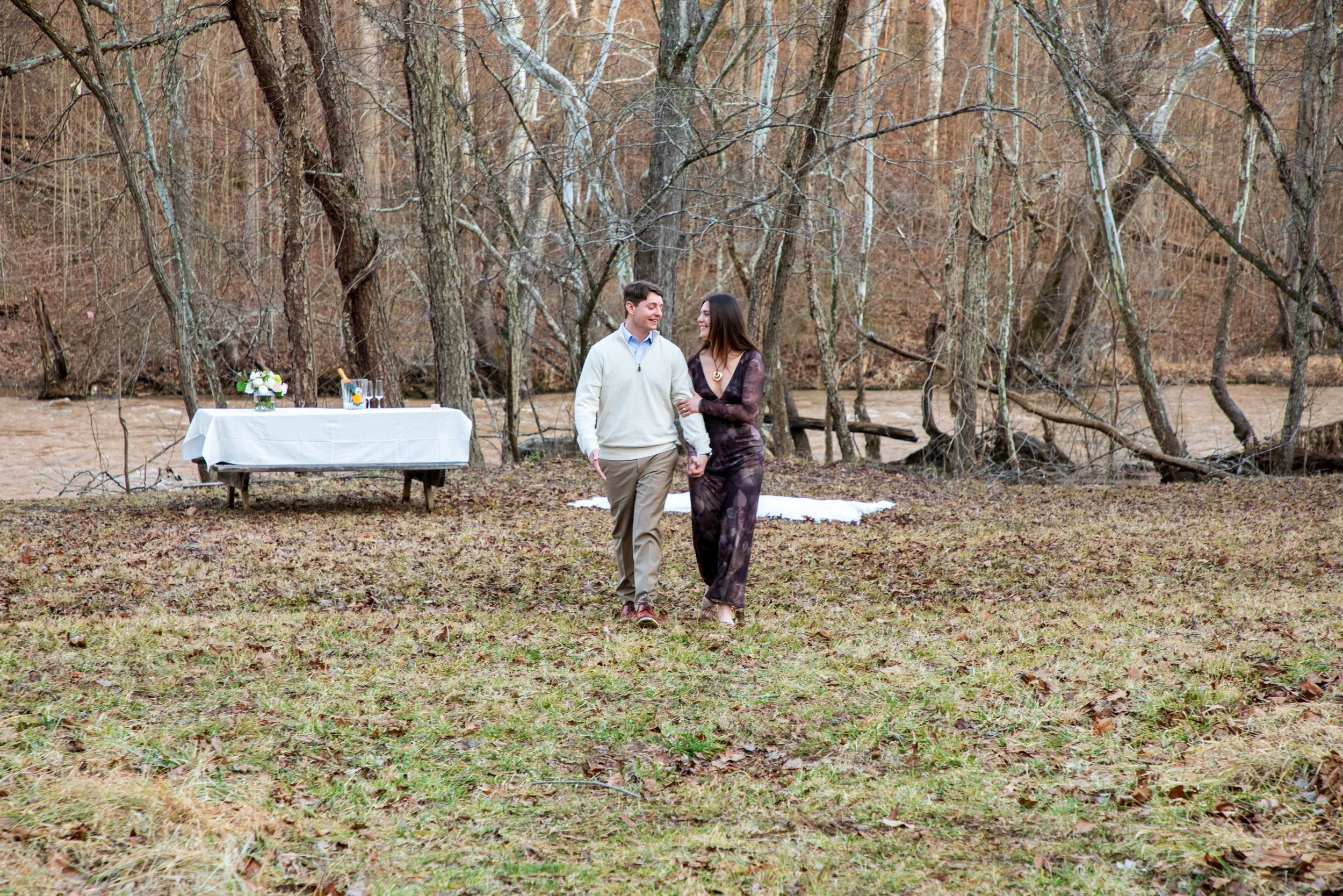 Engagement Photography by Will Locke near Richmond, VA in Montpelier. A couple walks while holding hands, with trees and a river in the background.