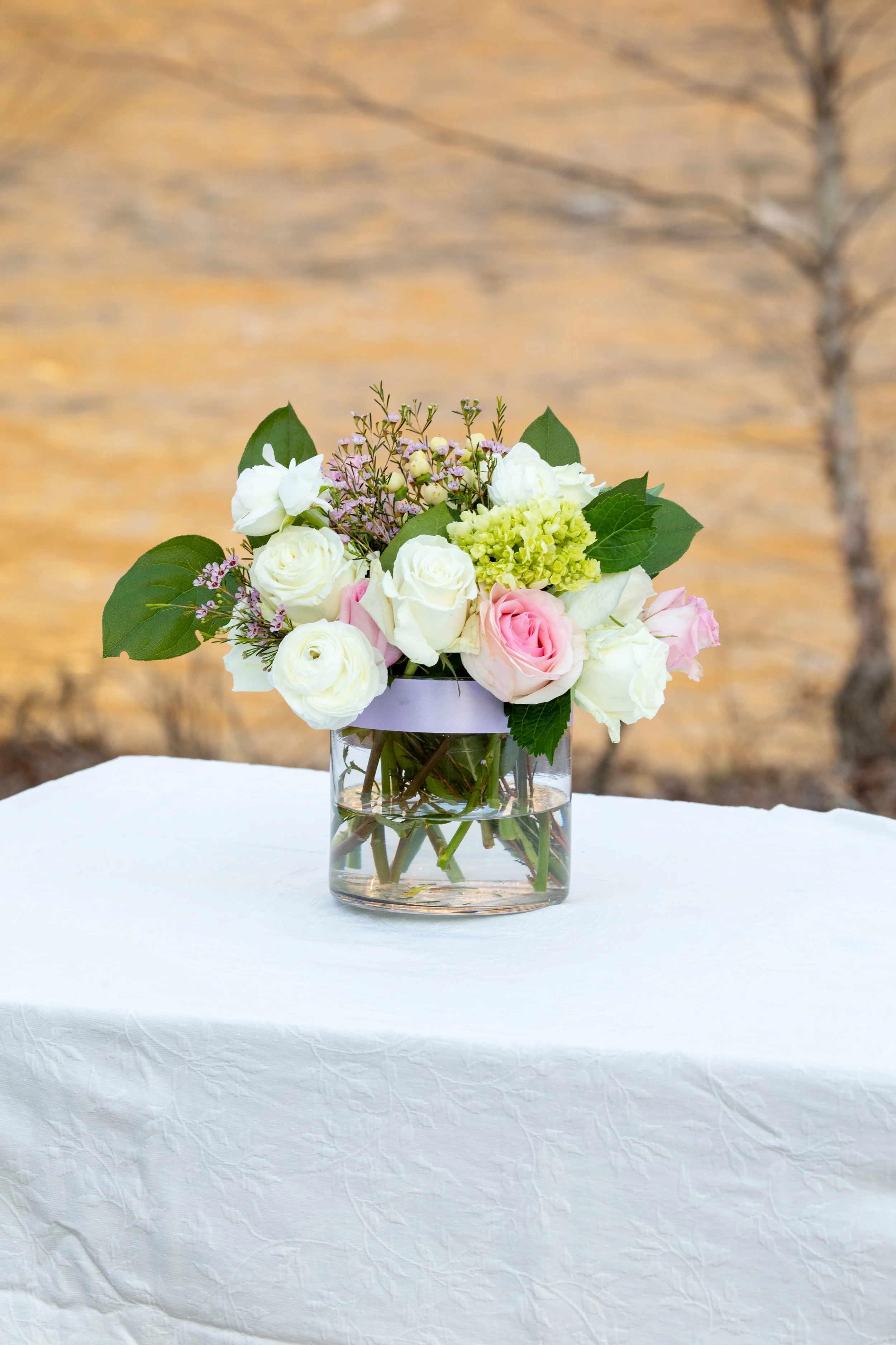 Engagement Photography by Will Locke near Richmond, VA in Montpelier. A flower arrangement sits on a white tablecloth outdoors in the winter with trees behind.