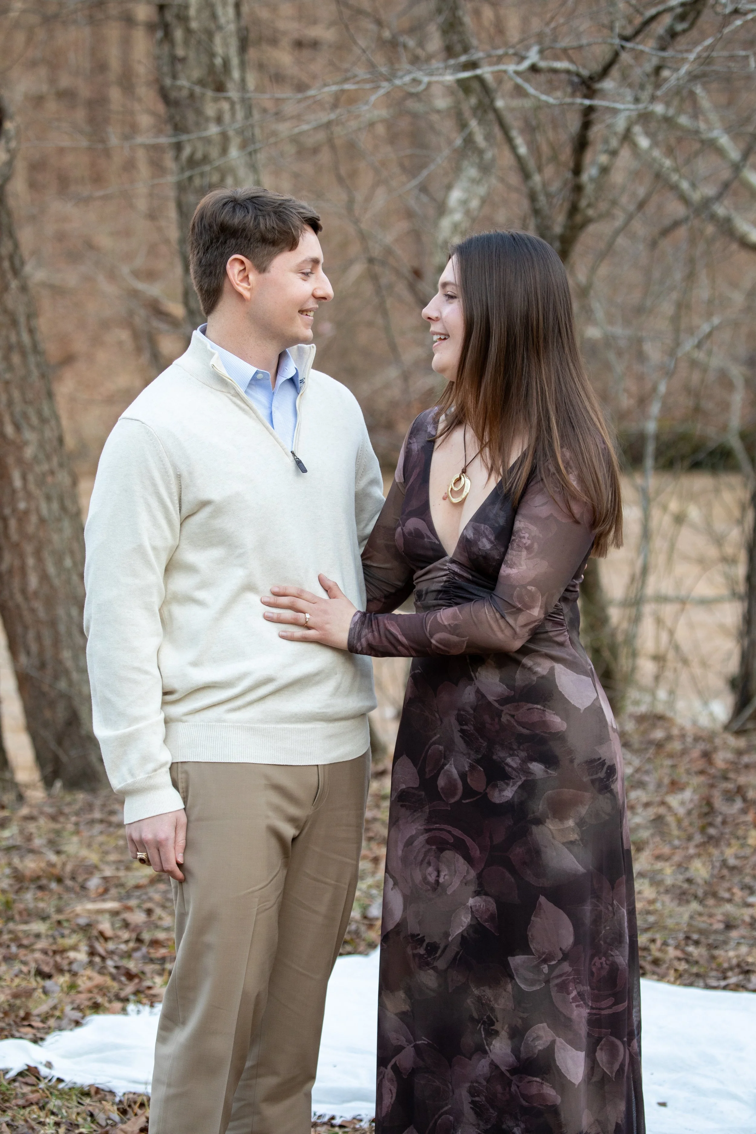 Engagement Photography by Will Locke near Richmond, VA in Montpelier. A man and woman smiling at each other while holding champagne glasses outdoors during sunset, with a table of flowers nearby.