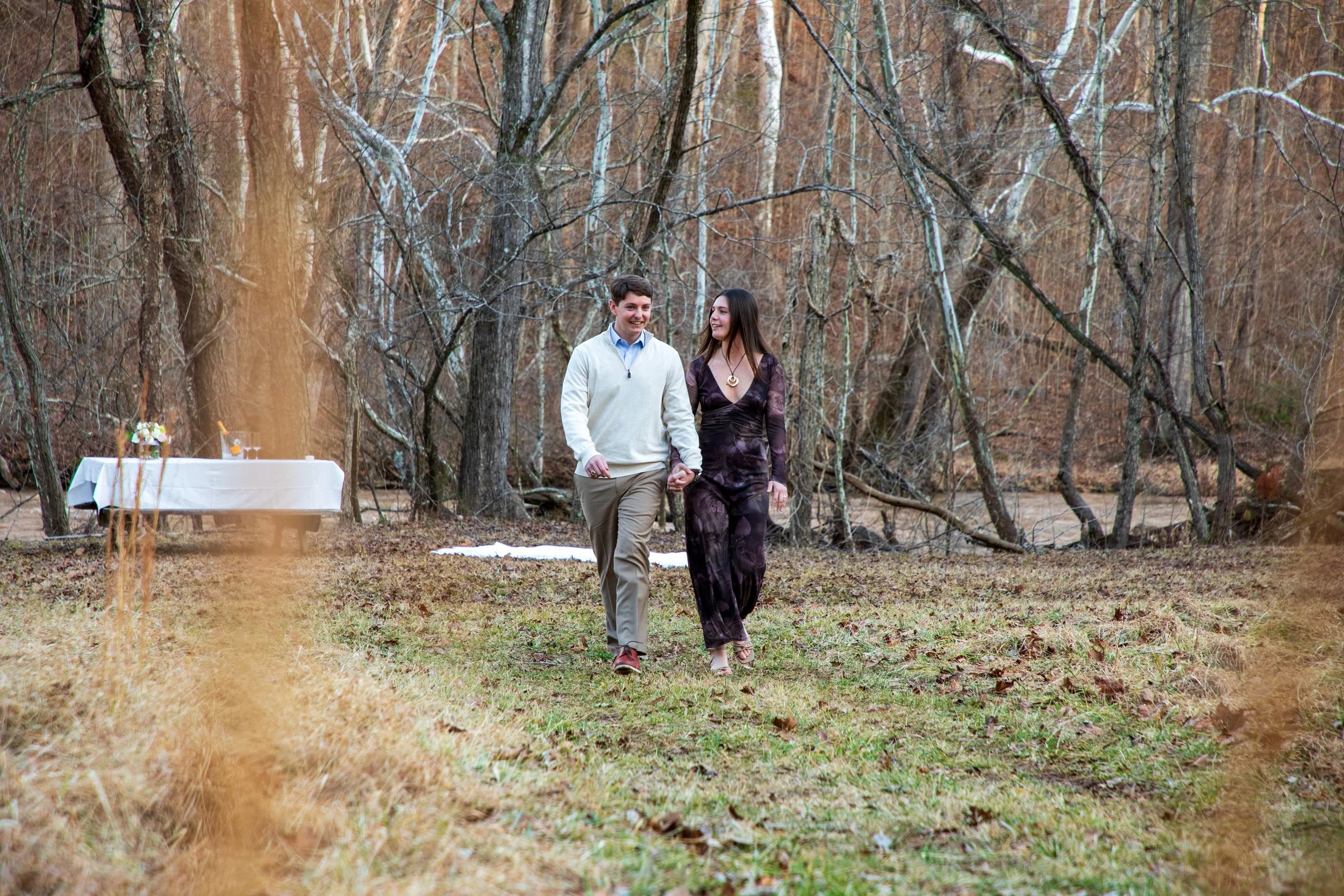 Engagement Photography by Will Locke near Richmond, VA in Montpelier. A couple walks while holding hands, with trees and a river in the background.