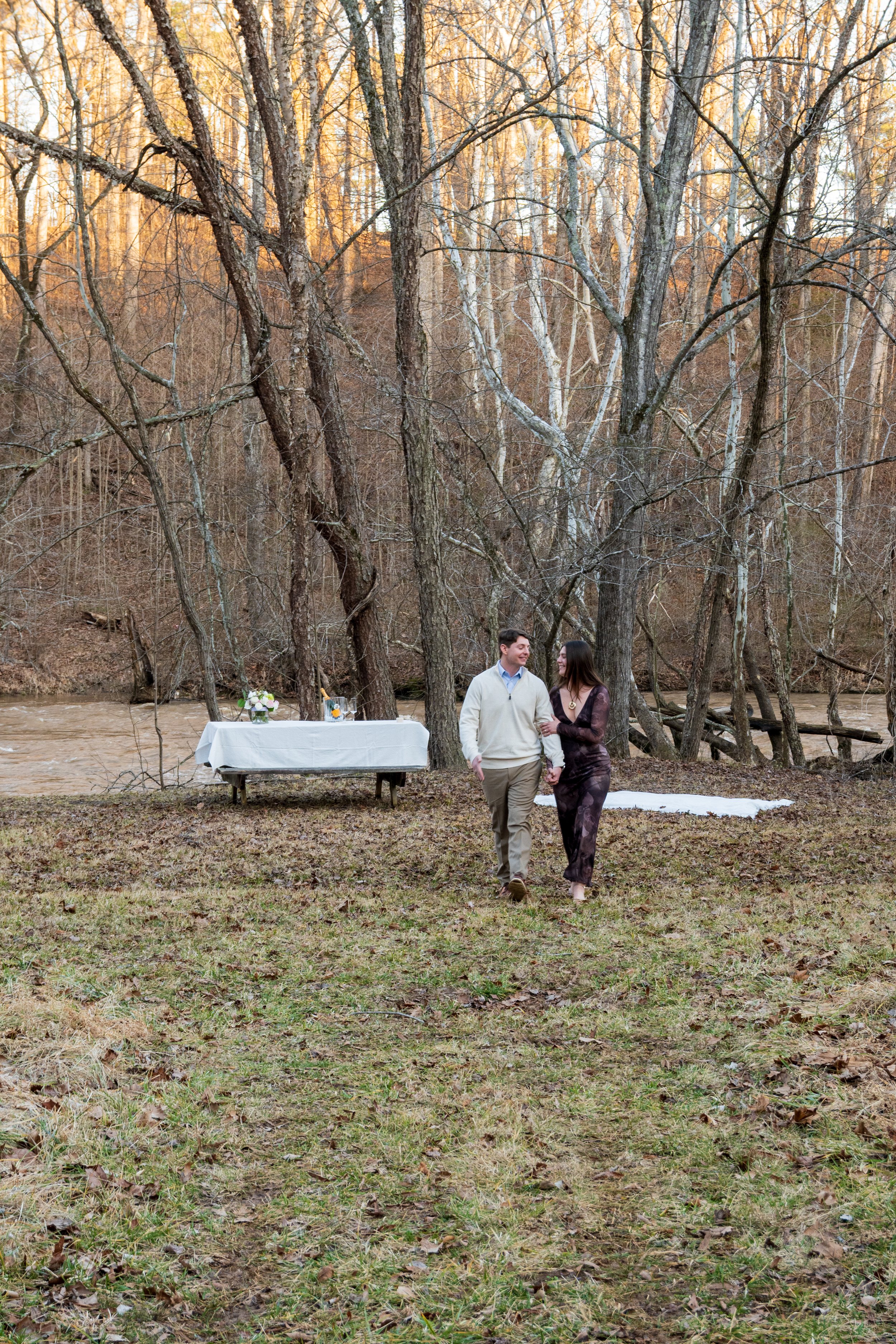 Engagement Photography by Will Locke near Richmond, VA in Montpelier. A couple walks while holding hands, with trees and a river in the background.