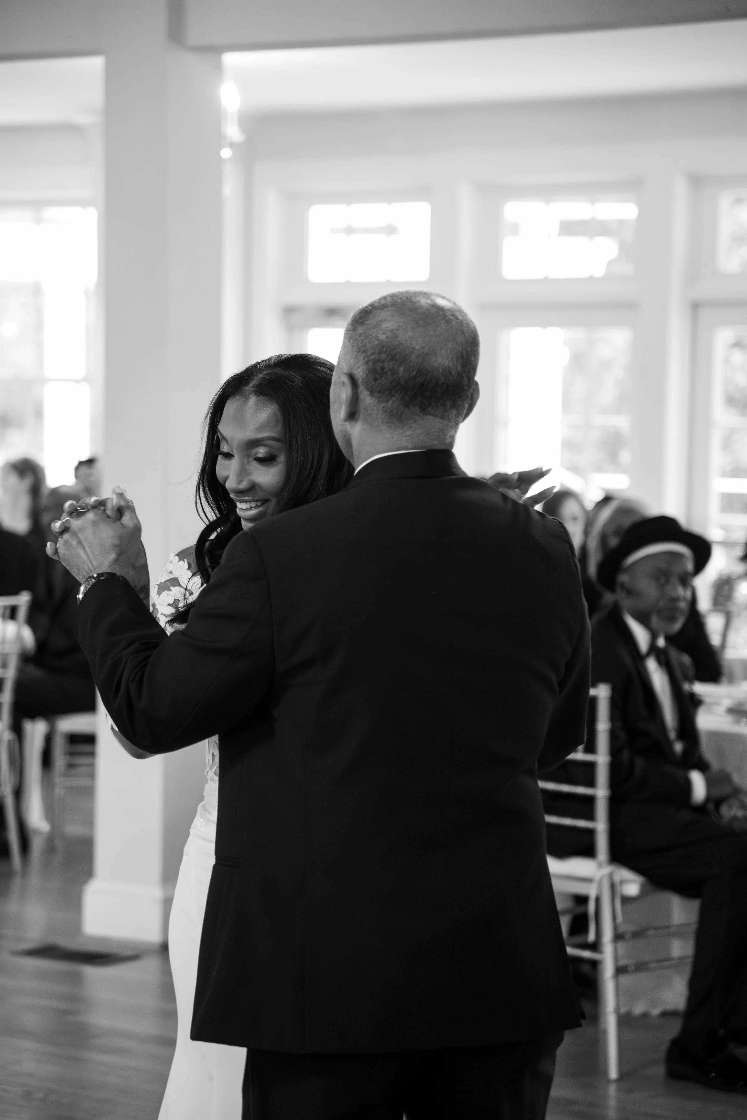 Wedding Photography by Will Locke. A woman and man dancing together at a wedding reception, with other guests seated and watching in the background.