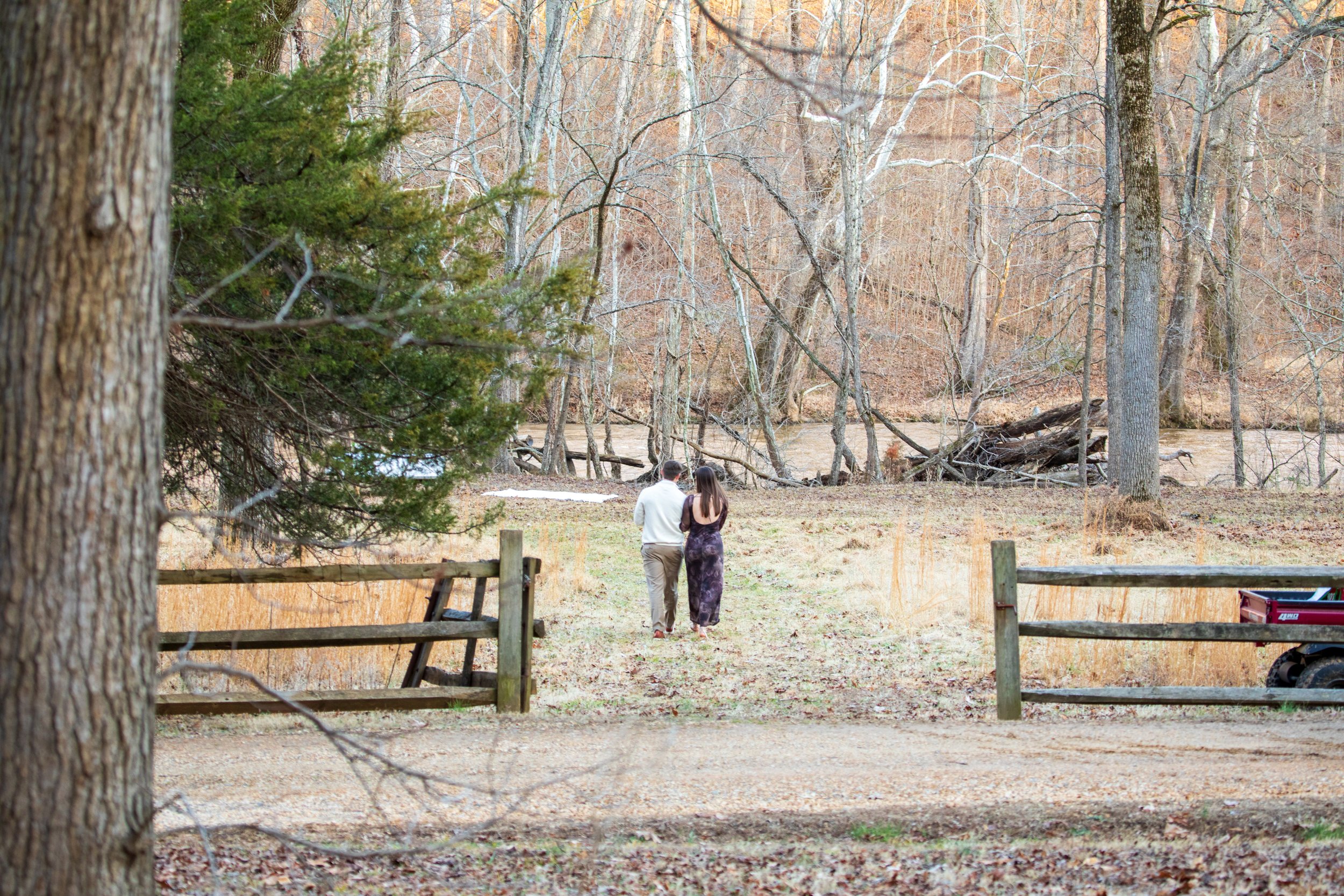 Engagement Photography by Will Locke near Richmond, VA in Montpelier. A couple walks on a white cloth on the ground near a wooded area with a stream on a fall day, with a table on the left side.