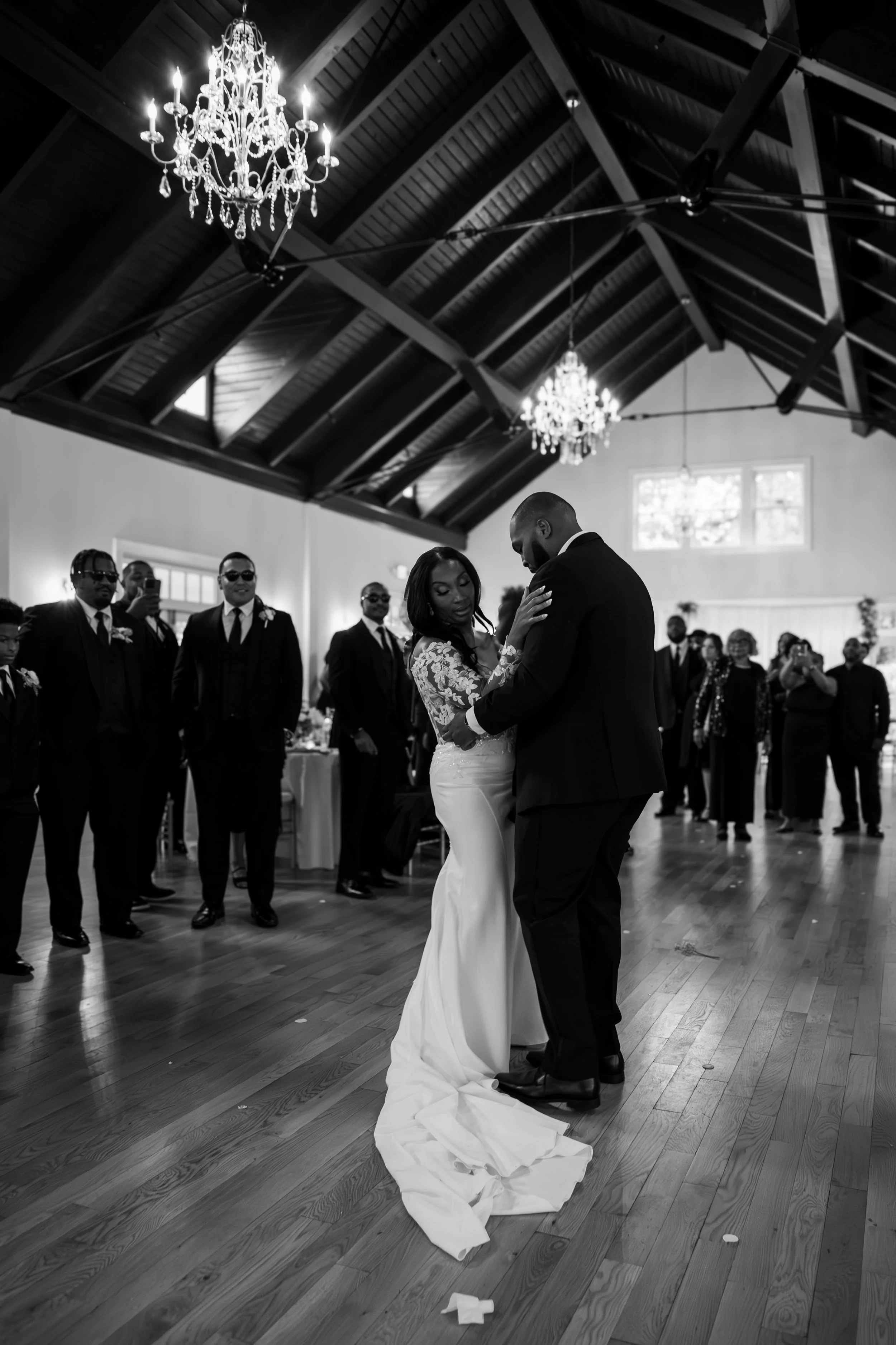 Photo & Video by Will Locke Wedding Photography at the Woman's Club of Portsmouth in Virginia. A bride and groom share their first dance at a wedding reception, surrounded by guests in a decorated venue with high wooden ceilings and chandeliers.
