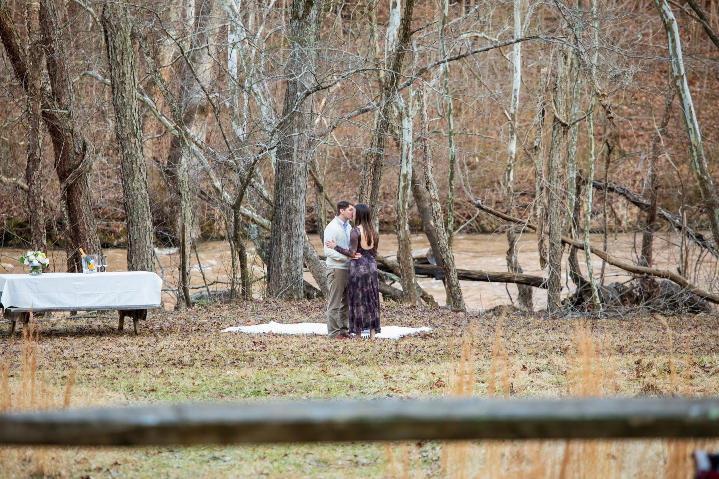 Engagement Photography by Will Locke near Richmond, VA in Montpelier. A couple appears to be engaged in an outdoor wedding ceremony by a river, with a table set up nearby.