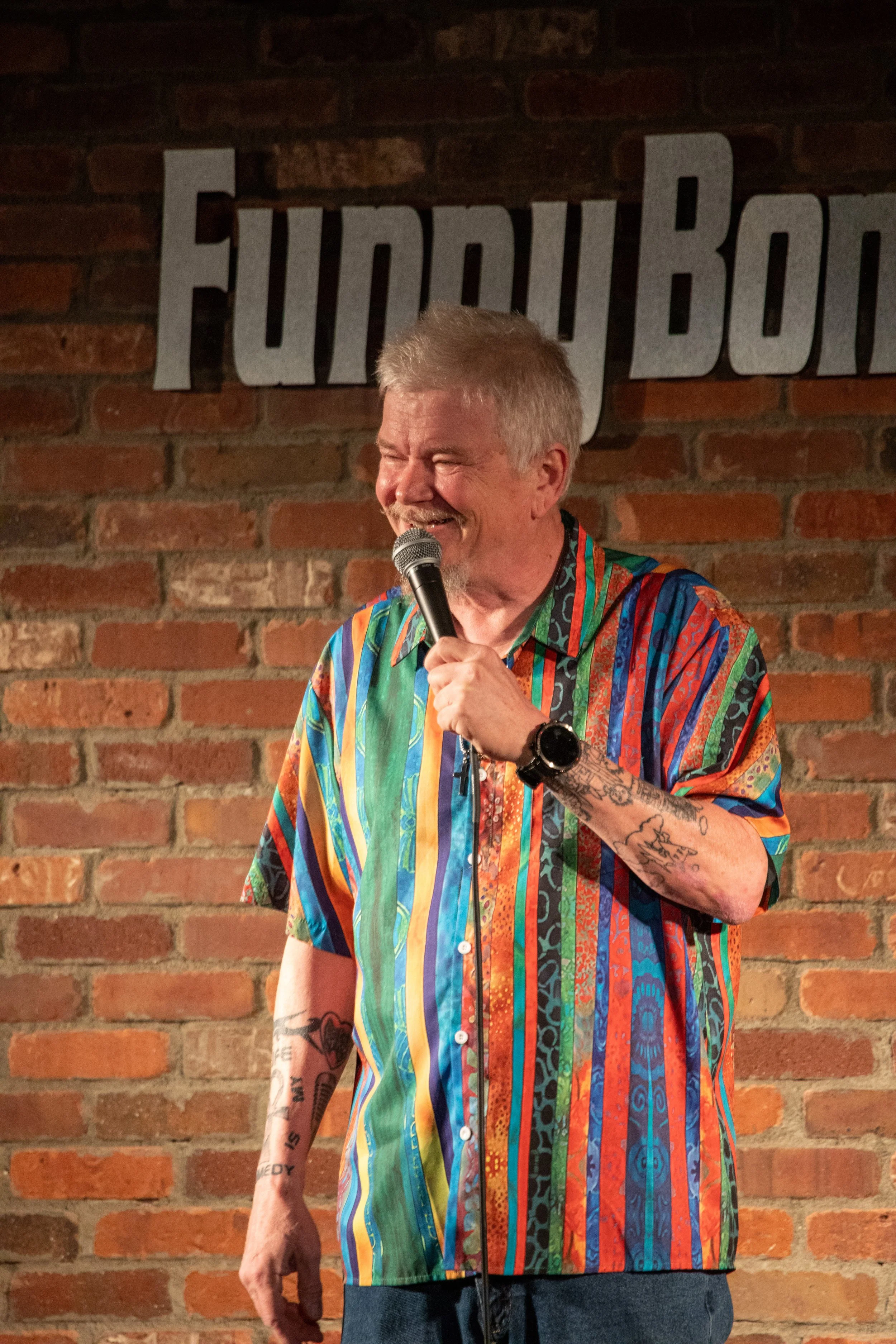 Comedy Photography by Will Locke in Norfolk, VA va male comedian wit gray hair and mustache holds microphone and smiles while performing. 