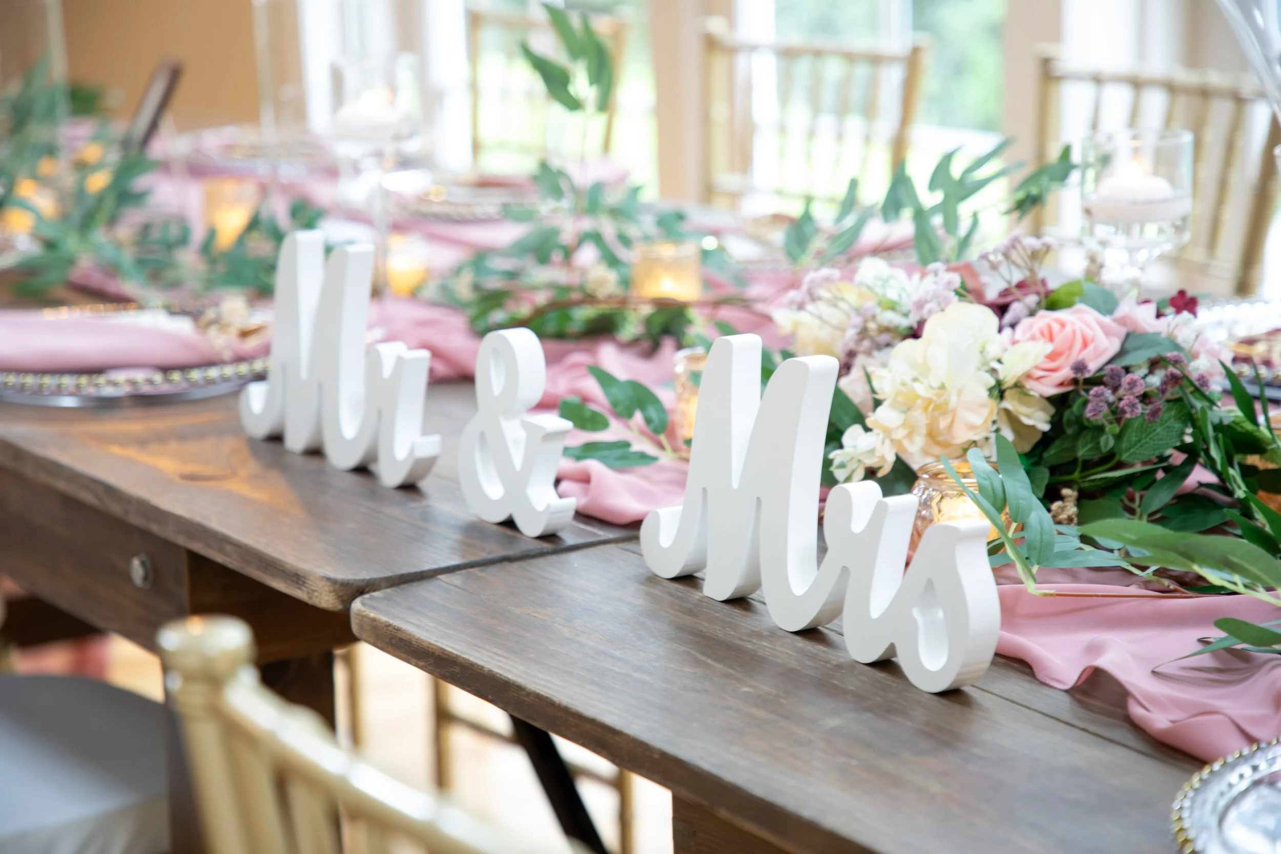 Wedding Photography by Will Locke. Decorated wedding reception table with pink tablecloth, floral arrangements, and a wooden 'Mr & Mrs' sign.