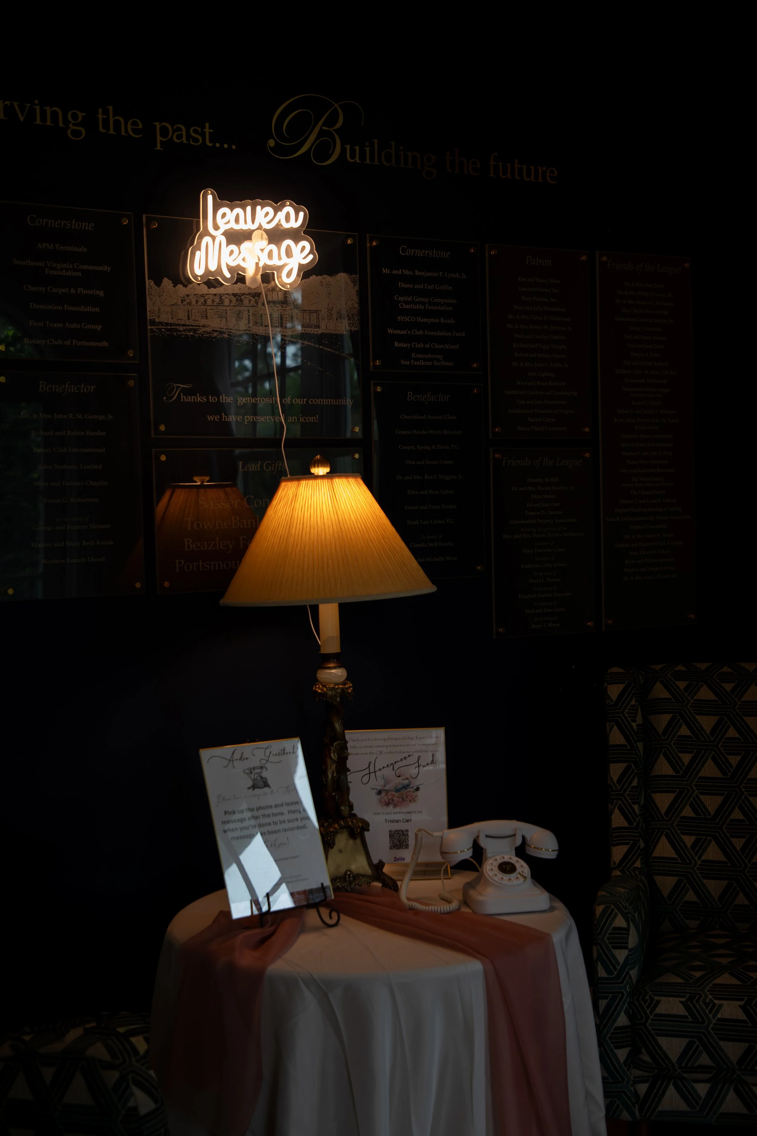 A dimly lit lobby area with a table featuring a vintage telephone and framed handwritten notes. A lit table lamp with a decorative base is prominent. Wedding Photography by Will Locke. 