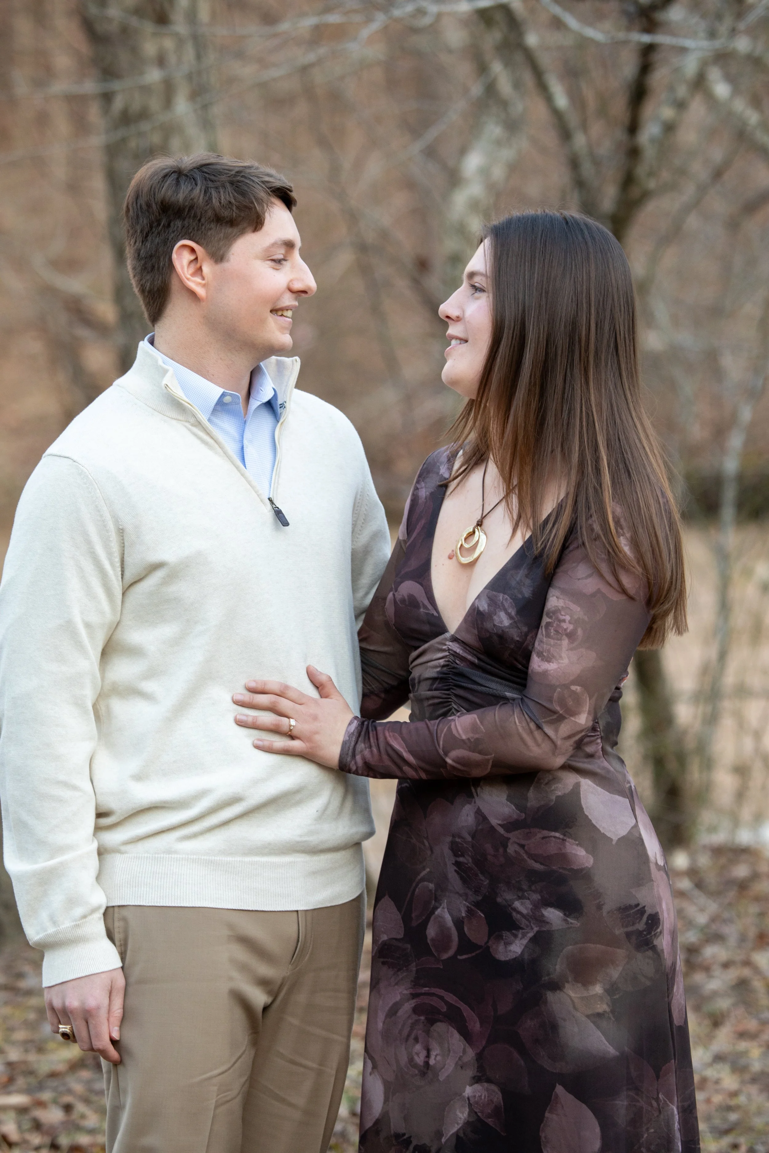 Engagement Photography by Will Locke near Richmond, VA in Montpelier. A man and woman smiling at each other while holding champagne glasses outdoors during sunset, with a table of flowers nearby.