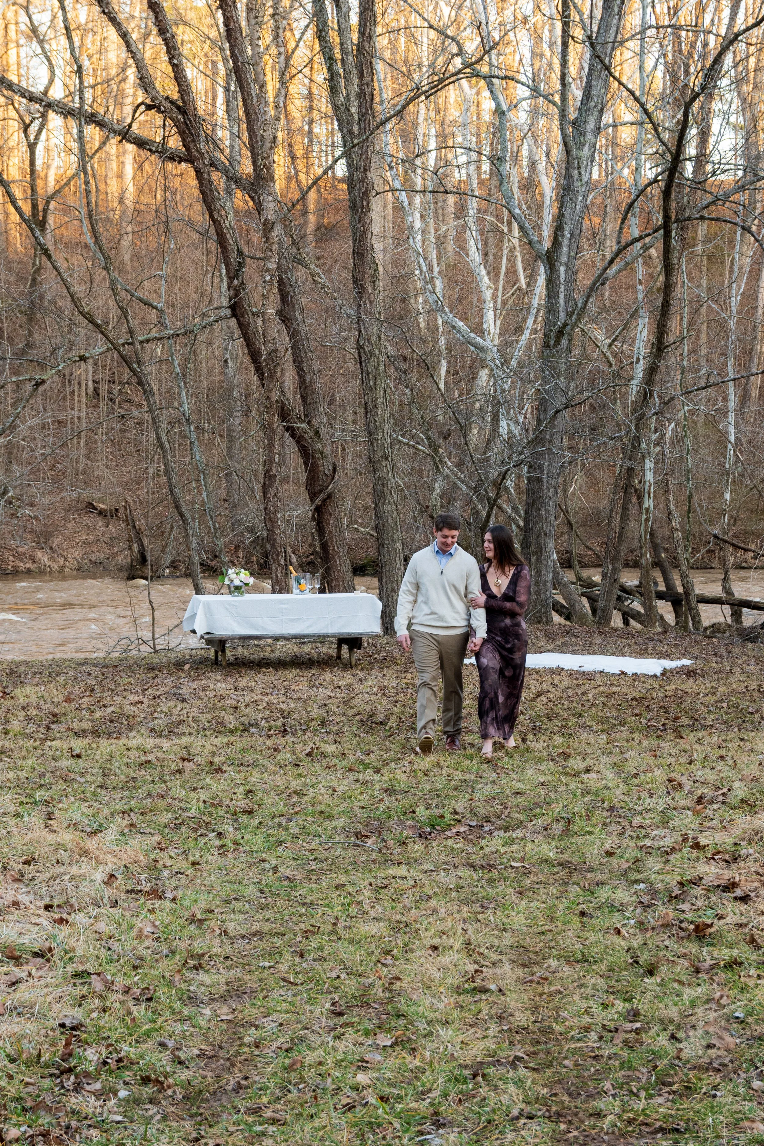 Engagement Photography by Will Locke near Richmond, VA in Montpelier. A couple walks while holding hands, with trees and a river in the background.