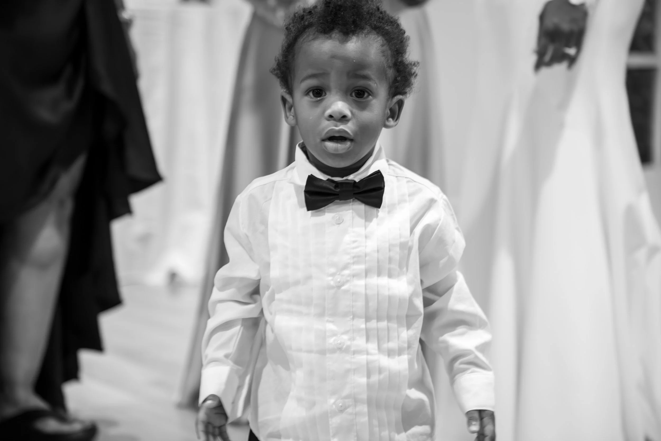 Photo & Video by Will Locke Wedding Photography at the Woman's Club of Portsmouth in Virginia. A young boy dressed in a white shirt with vertical stripes, a black bow tie, and dark pants, at a wedding.