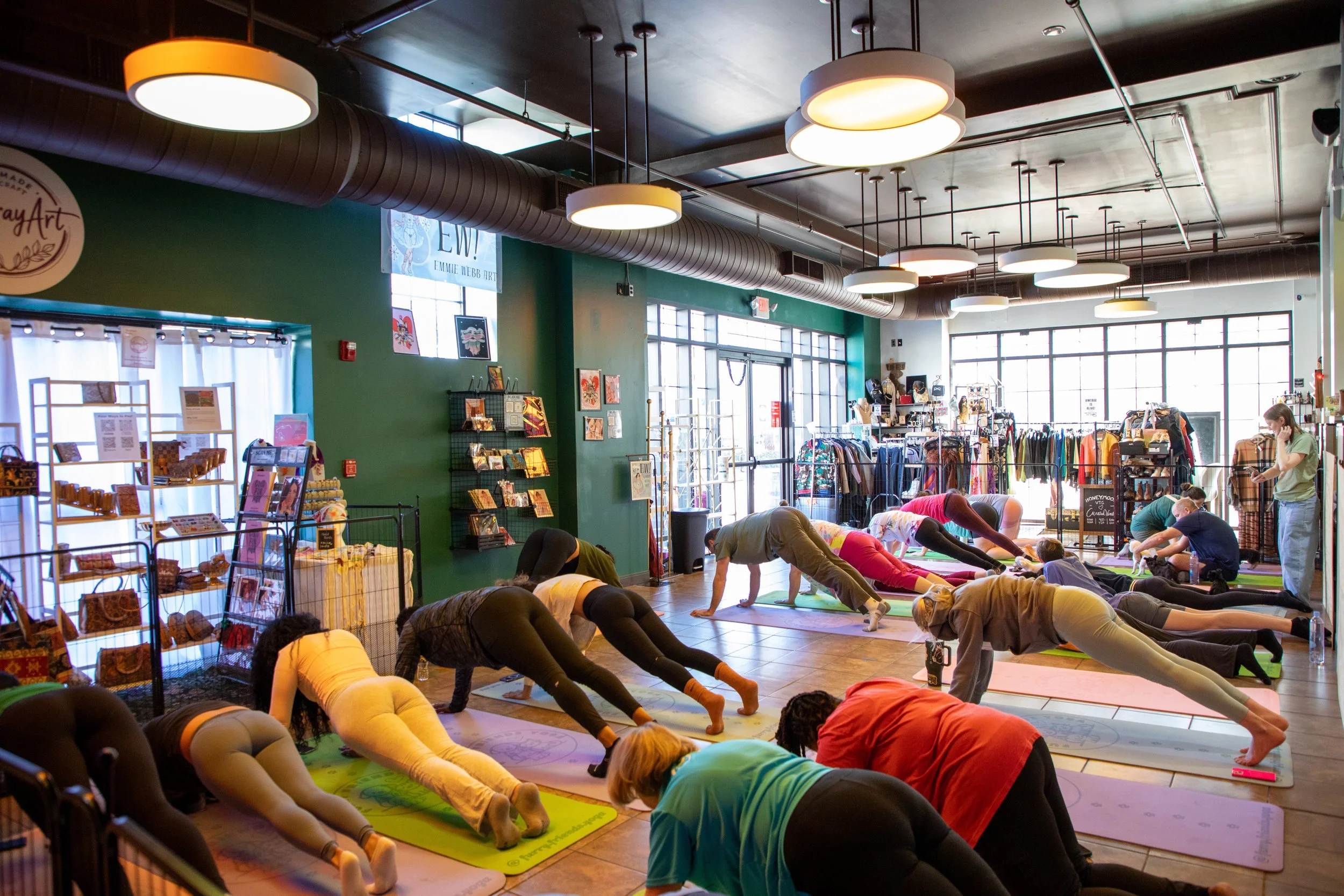 Marketing and Event Photography by Will Locke. People participating in a yoga class inside a retail store, practicing downward dog pose on yoga mats, with workout apparel and accessories on racks and shelves around them.