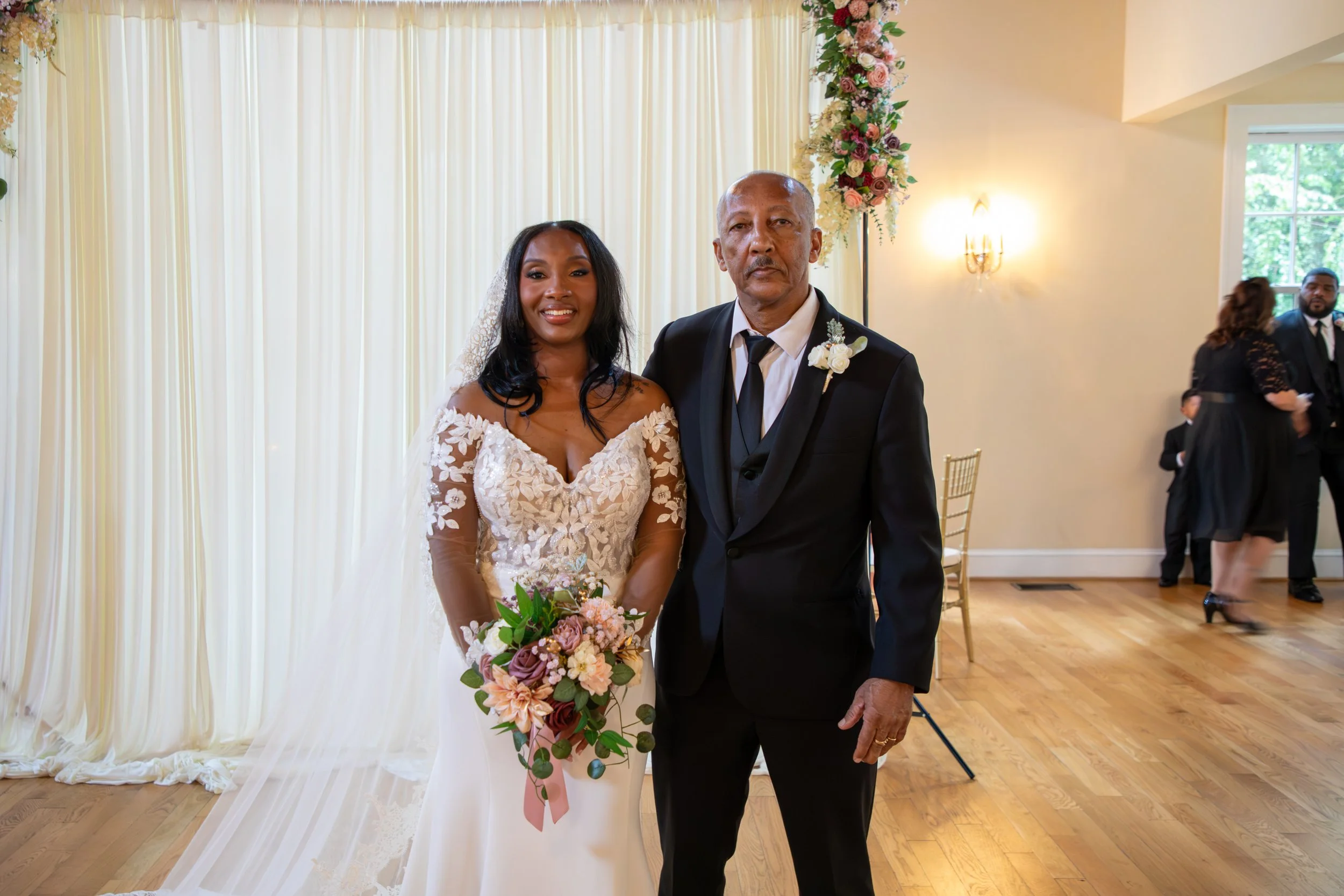Photo & Video by Will Locke Wedding Photography at the Woman's Club of Portsmouth in Virginia. A bride in a white wedding dress holding a bouquet, standing next to an older man in a black suit, in a decorated wedding venue.