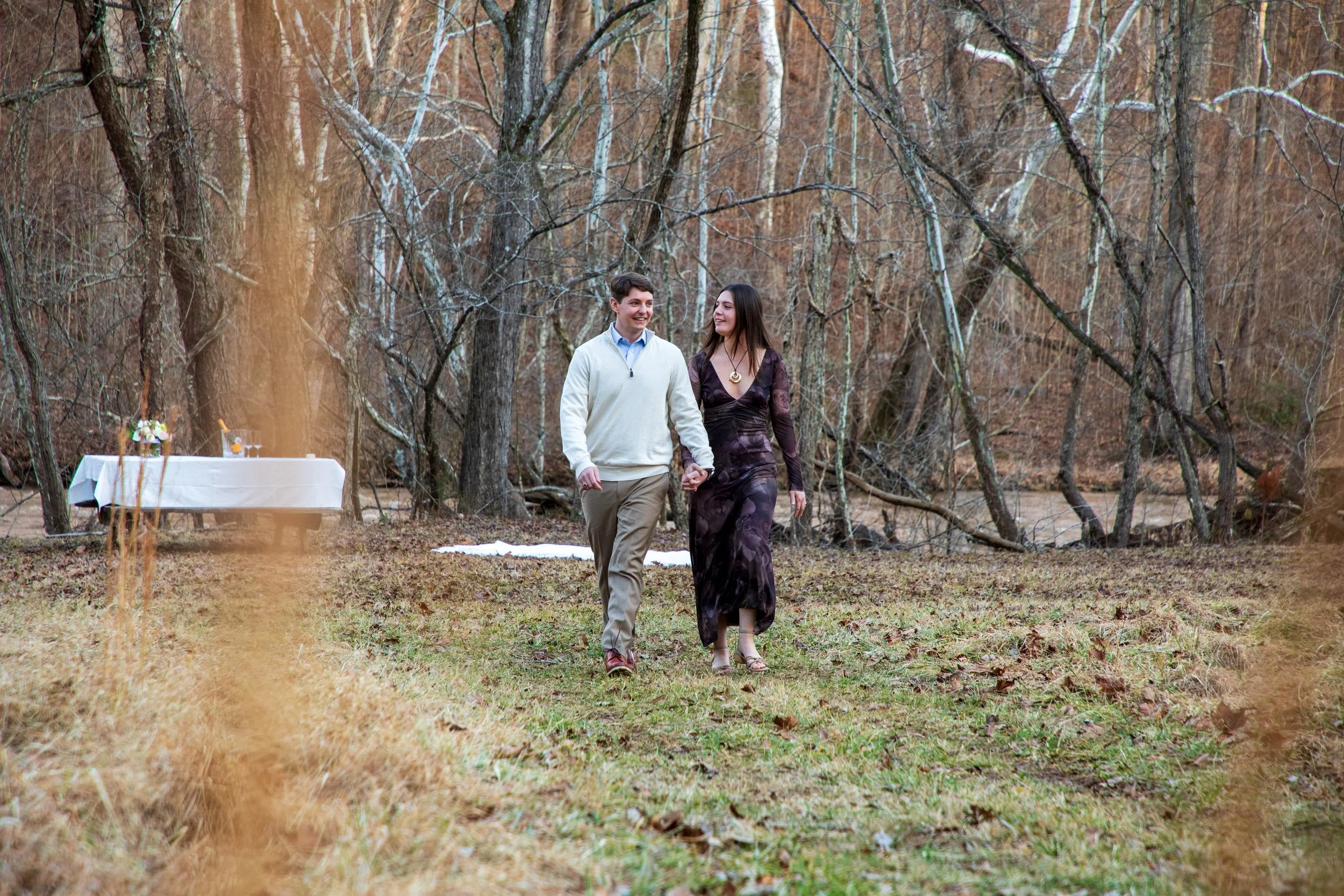 Engagement Photography by Will Locke near Richmond, VA in Montpelier. A couple walks while holding hands, with trees and a river in the background.