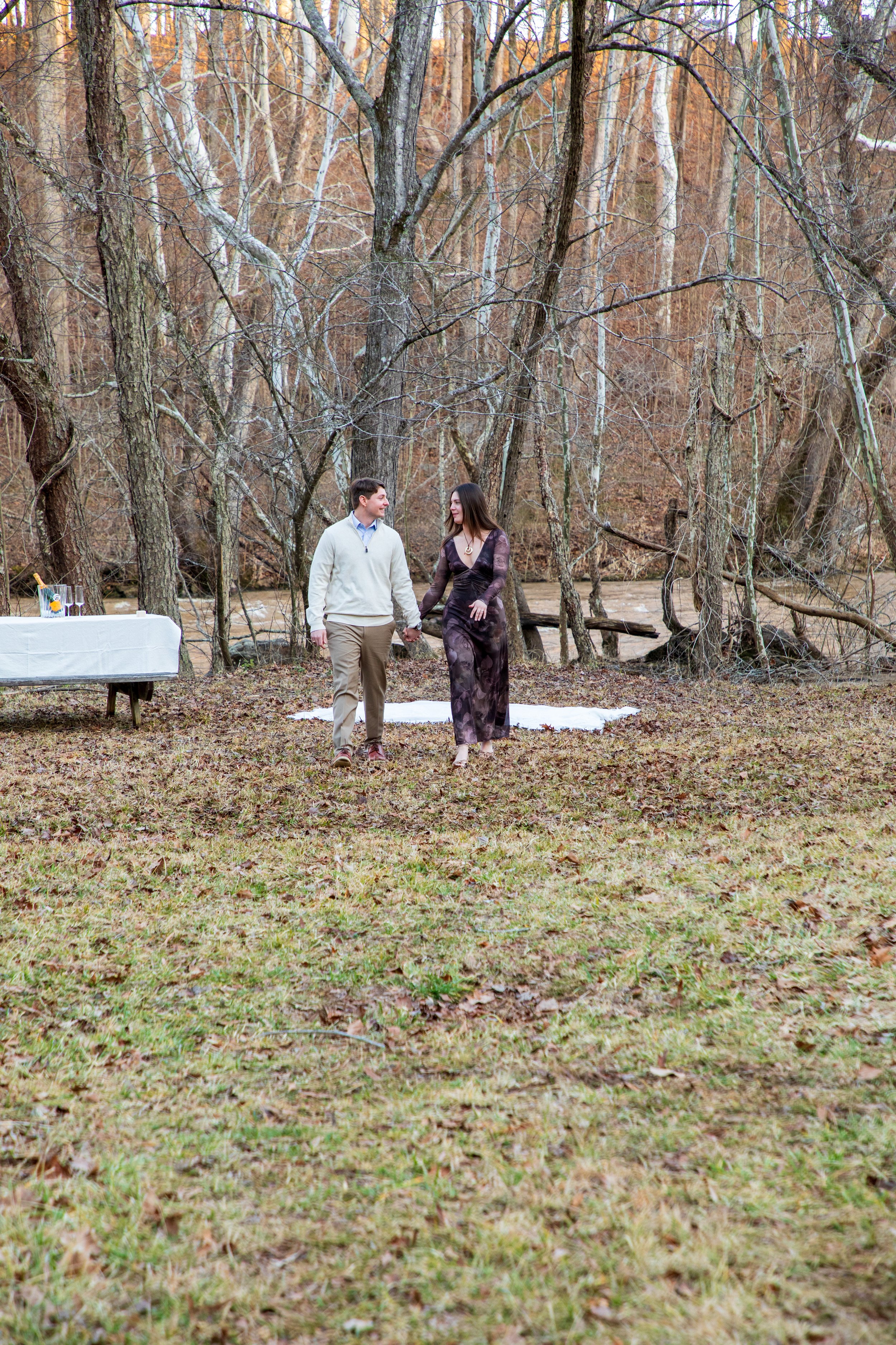 Engagement Photography by Will Locke near Richmond, VA in Montpelier. A couple walks while holding hands, with trees and a river in the background.