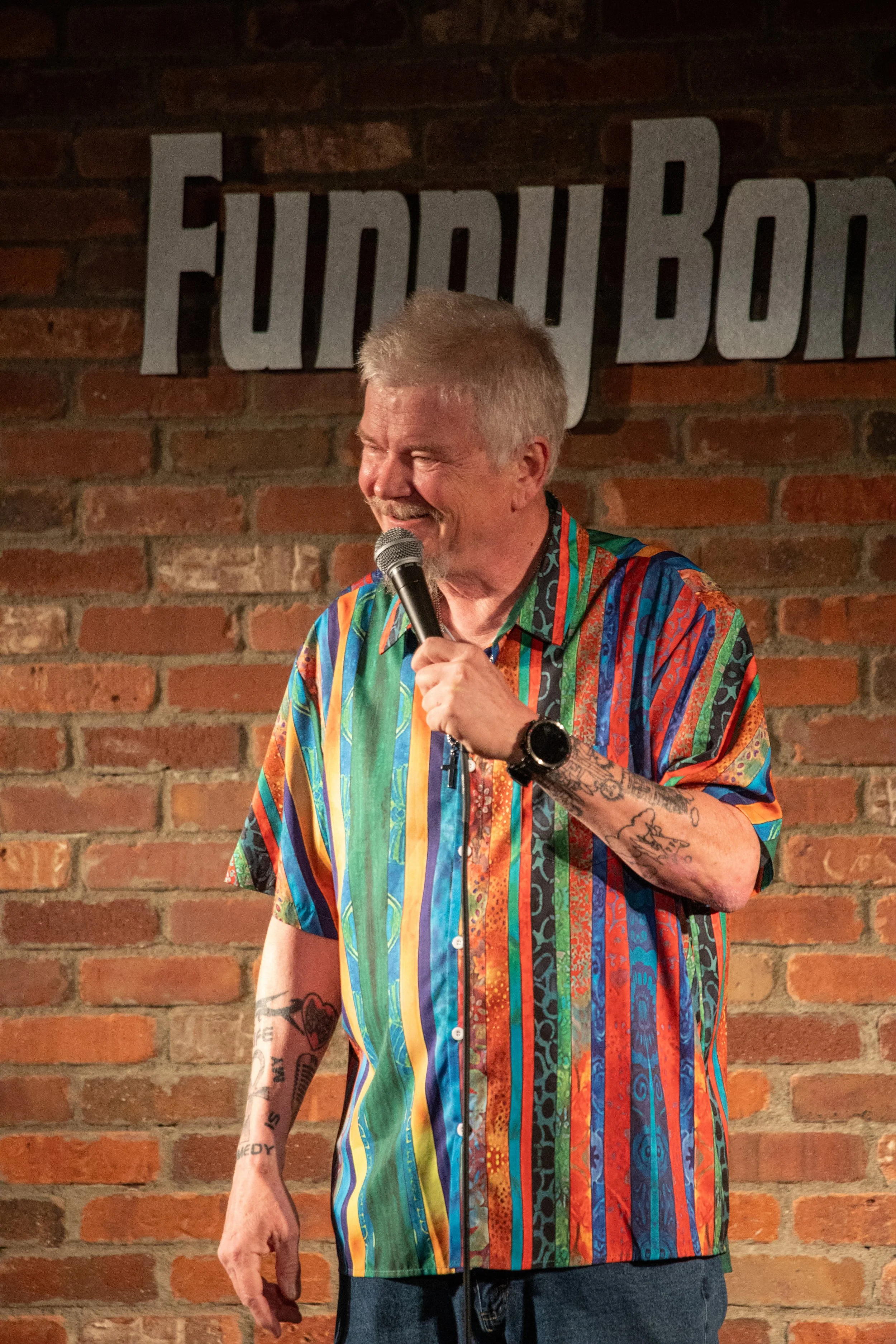 Comedy Photography by Will Locke in Norfolk, VA. Male comedian smiling while holding microphone and looking at crowd while performing.