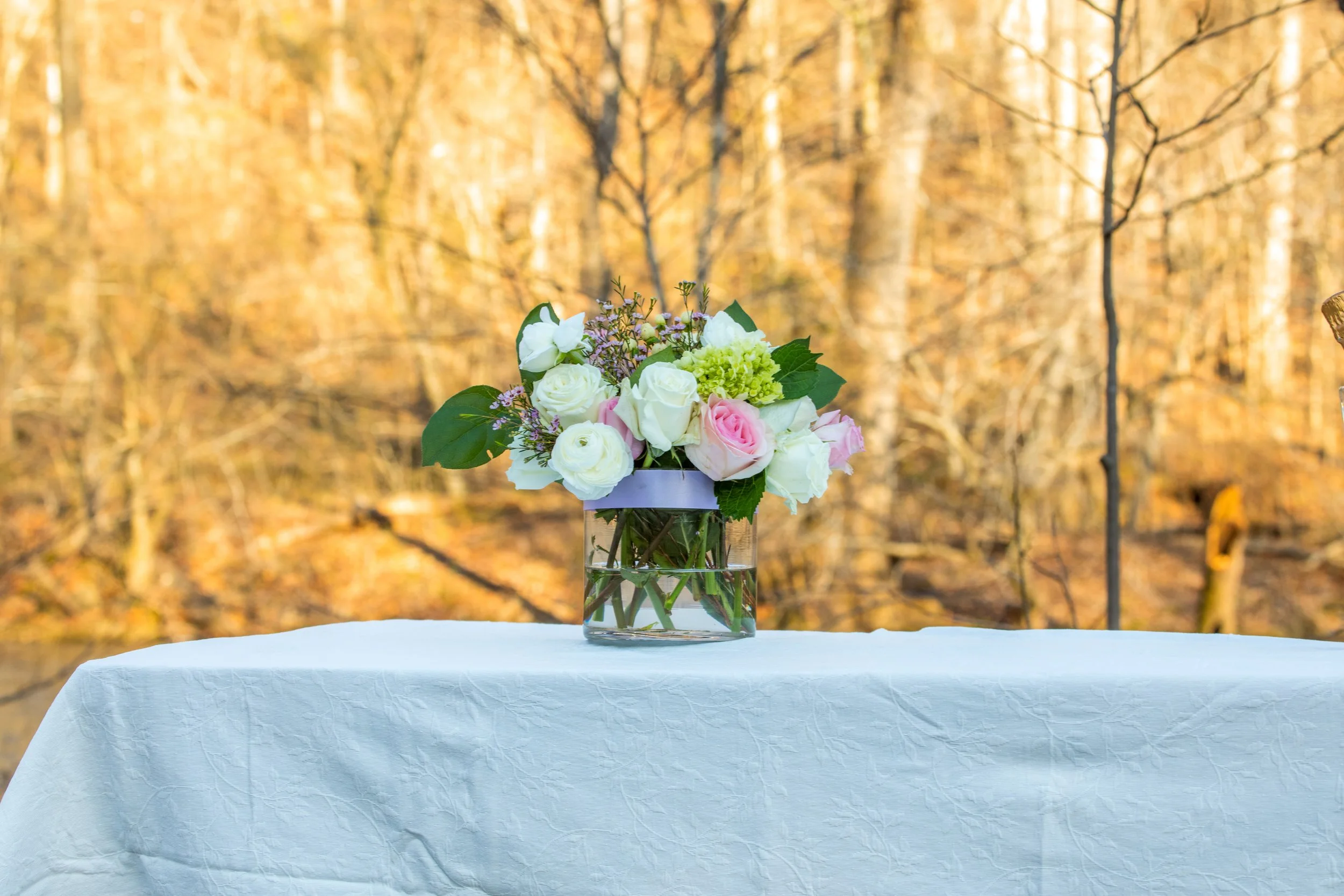 Engagement Photography by Will Locke near Richmond, VA in Montpelier. A flower arrangement sits on a white tablecloth outdoors in the winter with trees behind.