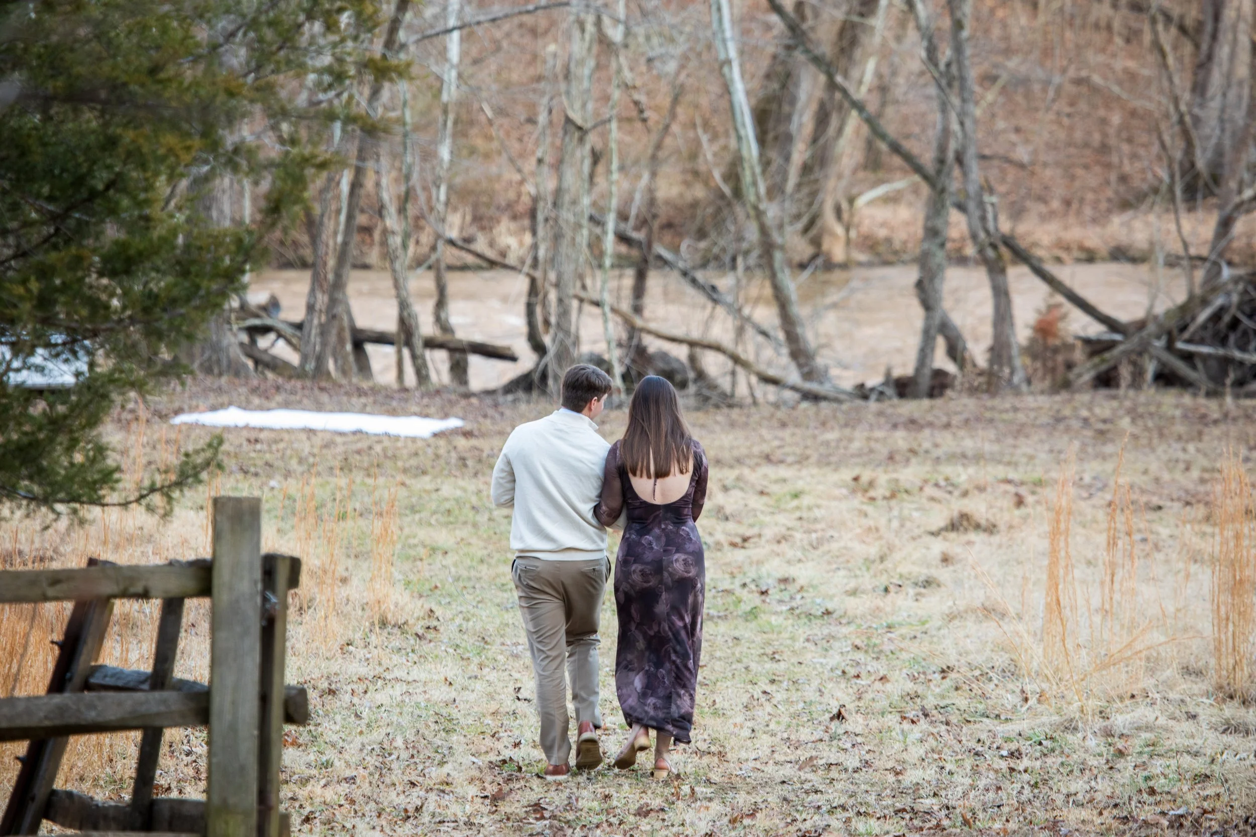 Engagement Photography by Will Locke near Richmond, VA in Montpelier. A couple walks to a white cloth on the ground near a wooded area with a stream on a fall day, with a table on the left side with white tablecloth.