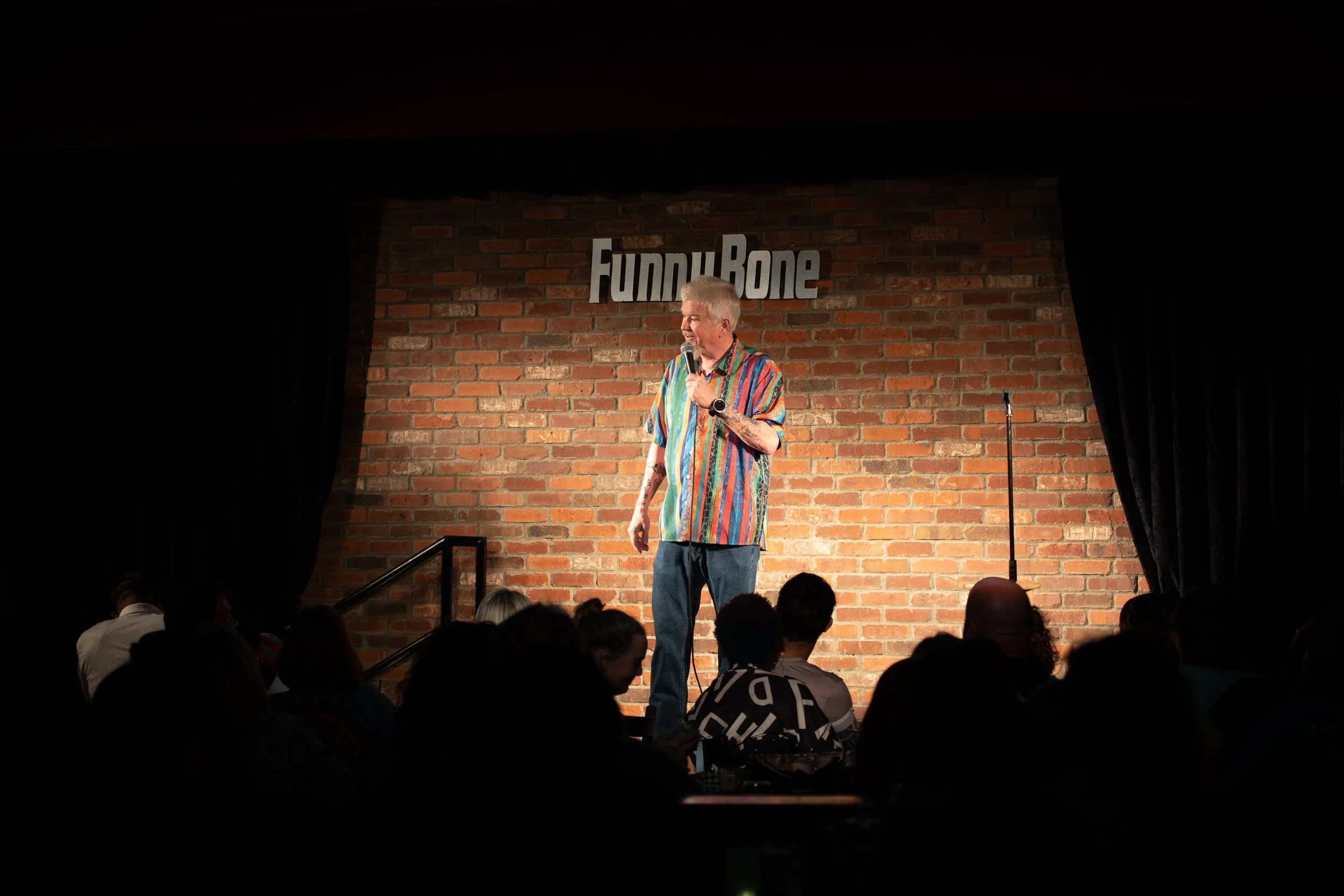 Comedy Photography by Will Locke in Norfolk, VA. A wideshot of a male comedian with colorful shirt holding a microphone while performing jokes on stage. 