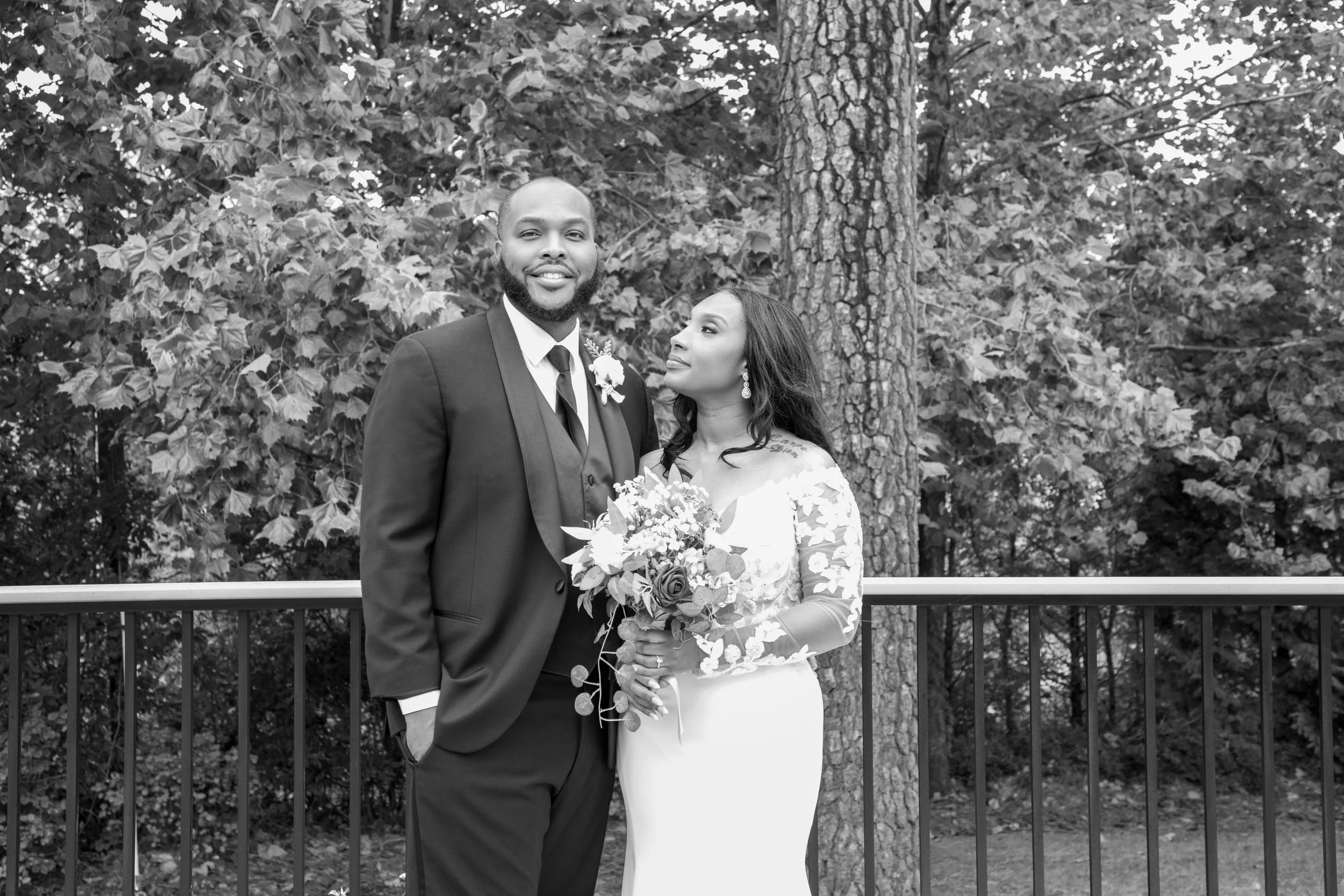 Photo & Video by Will Locke Wedding Photography at the Woman's Club of Portsmouth in Virginia. A black and white photo of a newlywed couple standing outdoors in front of trees.