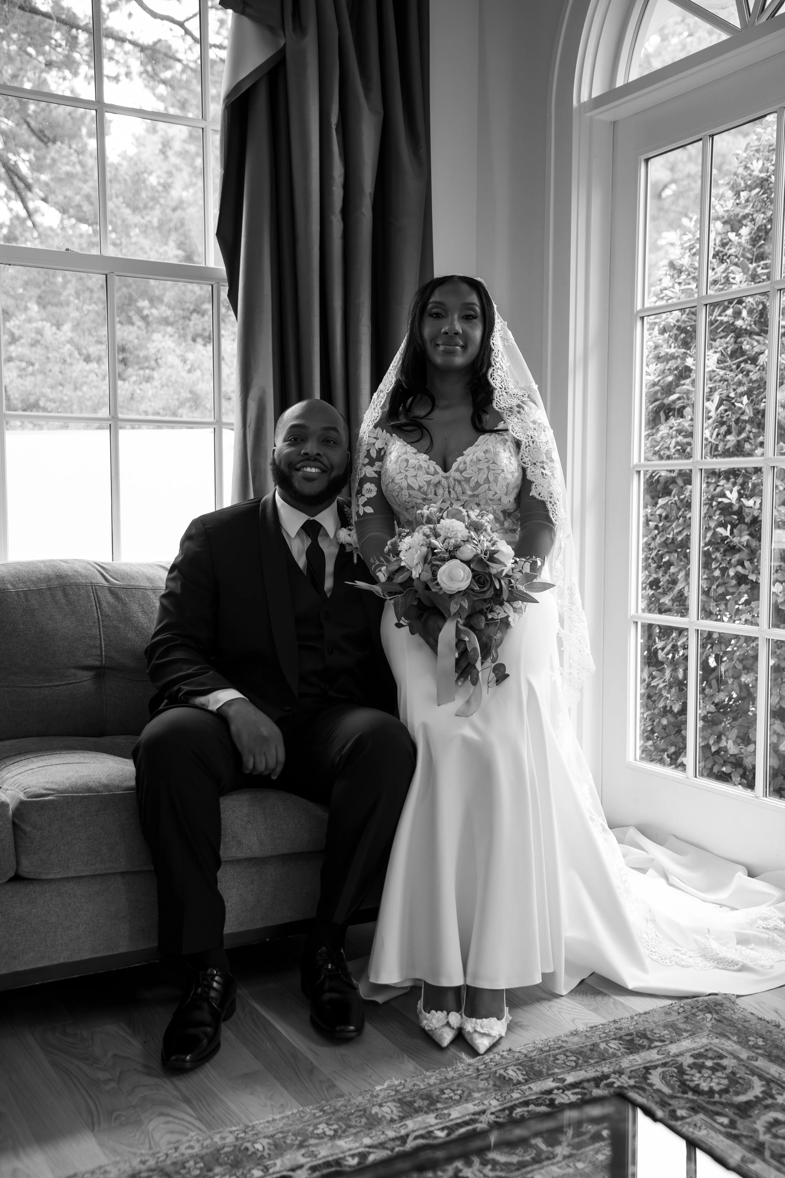 A bride and groom pose together inside a well-lit room, with large windows behind them. Photo & Video by Will Locke Wedding Photography at the Woman's Club of Portsmouth in Virginia. 