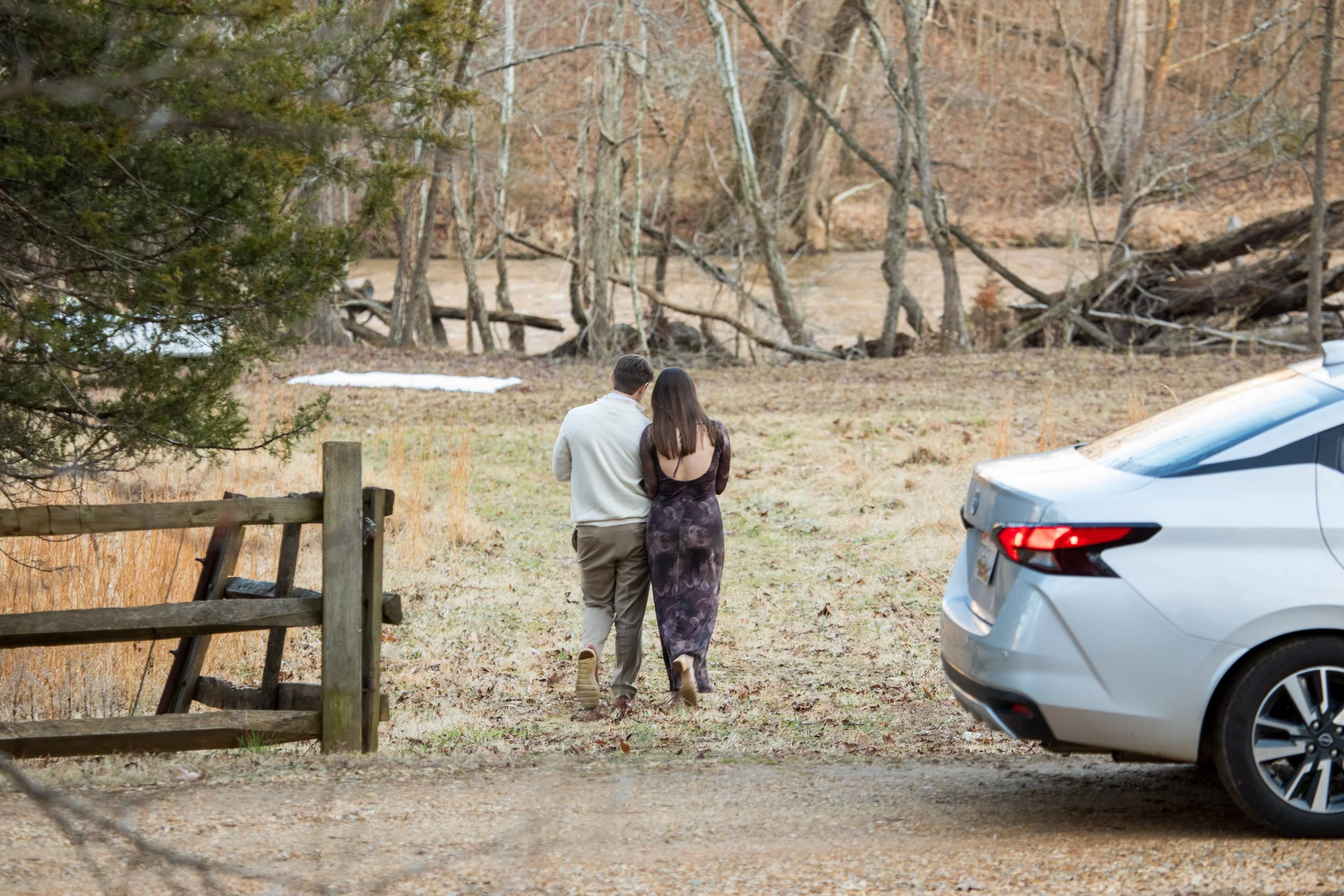 Engagement Photography by Will Locke near Richmond, VA in Montpelier. A couple walks to a white cloth on the ground near a wooded area with a stream on a fall day, with a table on the left side with white tablecloth.
