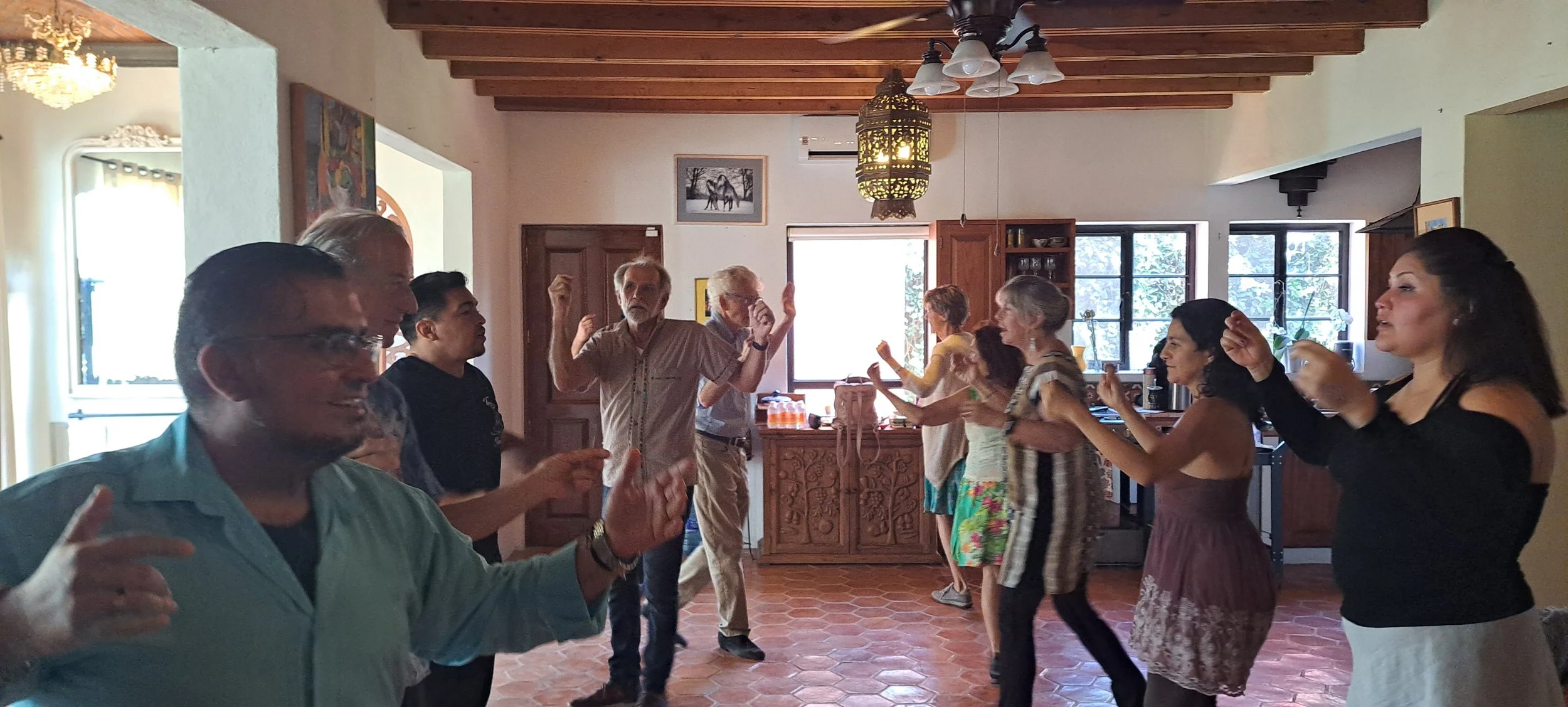 Group of people dancing and enjoying a celebration indoors with sunlight streaming through windows.