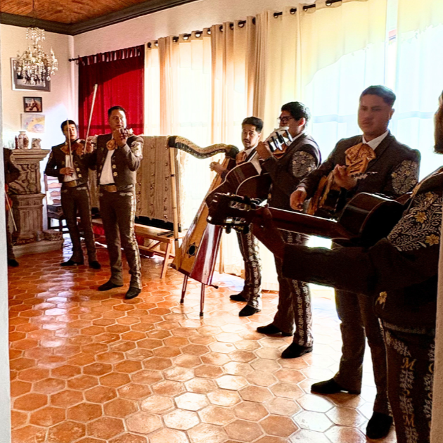 Mexican musicians playing traditional instruments indoors, dressed in matching embroidered suits.