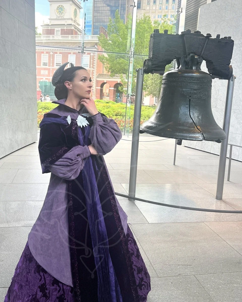 In front of the Liberty Bell in Philadelphia, she stands gazing to the side, right hand supporting left elbow, with her left hand under her chin. She wears the purple gown of Padmé Amidala's final senate appearance in Revenge of the Sith.