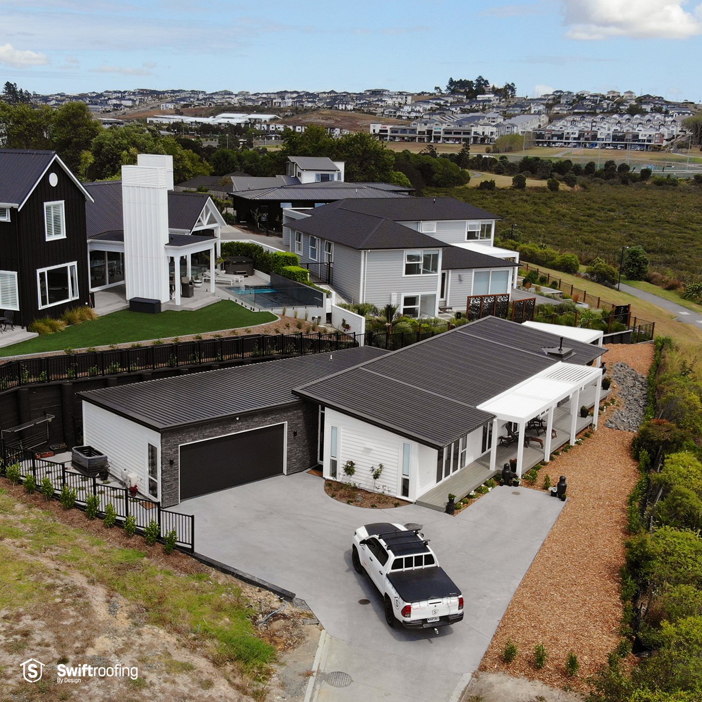 Pulled back drone view of garage and vehicle in front of Silver Medal House of the Year Winner where Swift Roofing installed Colorsteel Maxx coated, Flaxpod coloured Trimrib profile roofing.