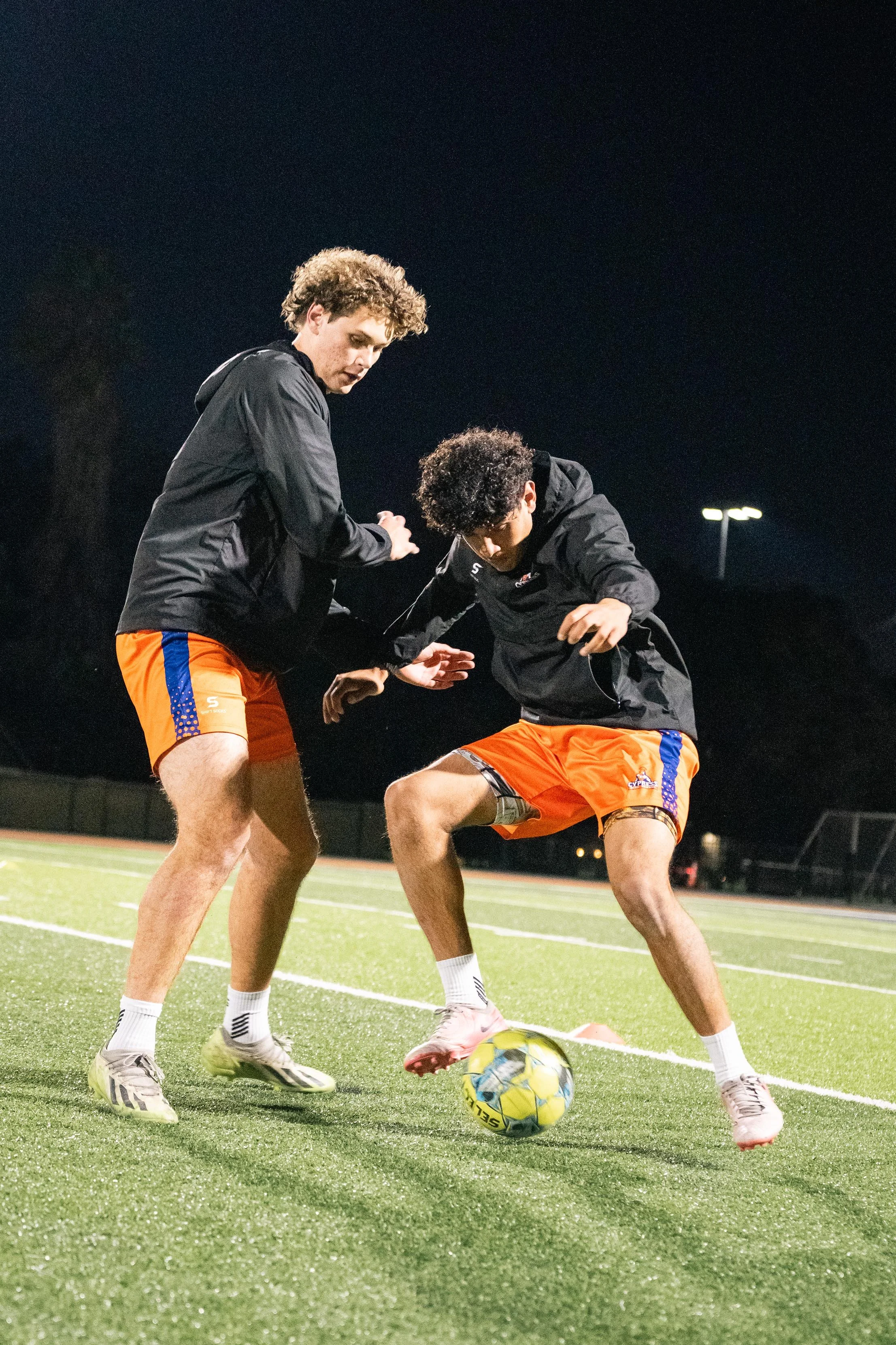 Two soccer players practicing on a field at night