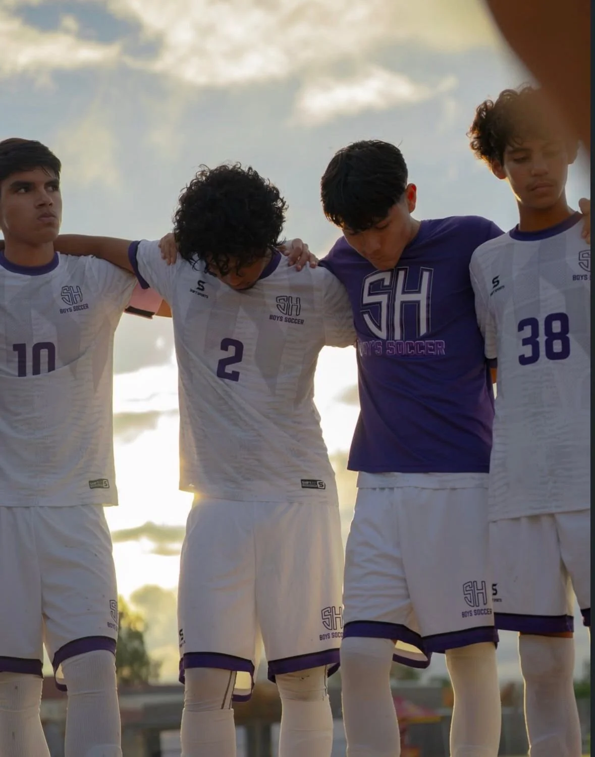 A group of young male athletes walking on a field with their sports gear, wearing black and blue uniforms with 'PANTHER' written on the front, carrying shoes and sports bags.