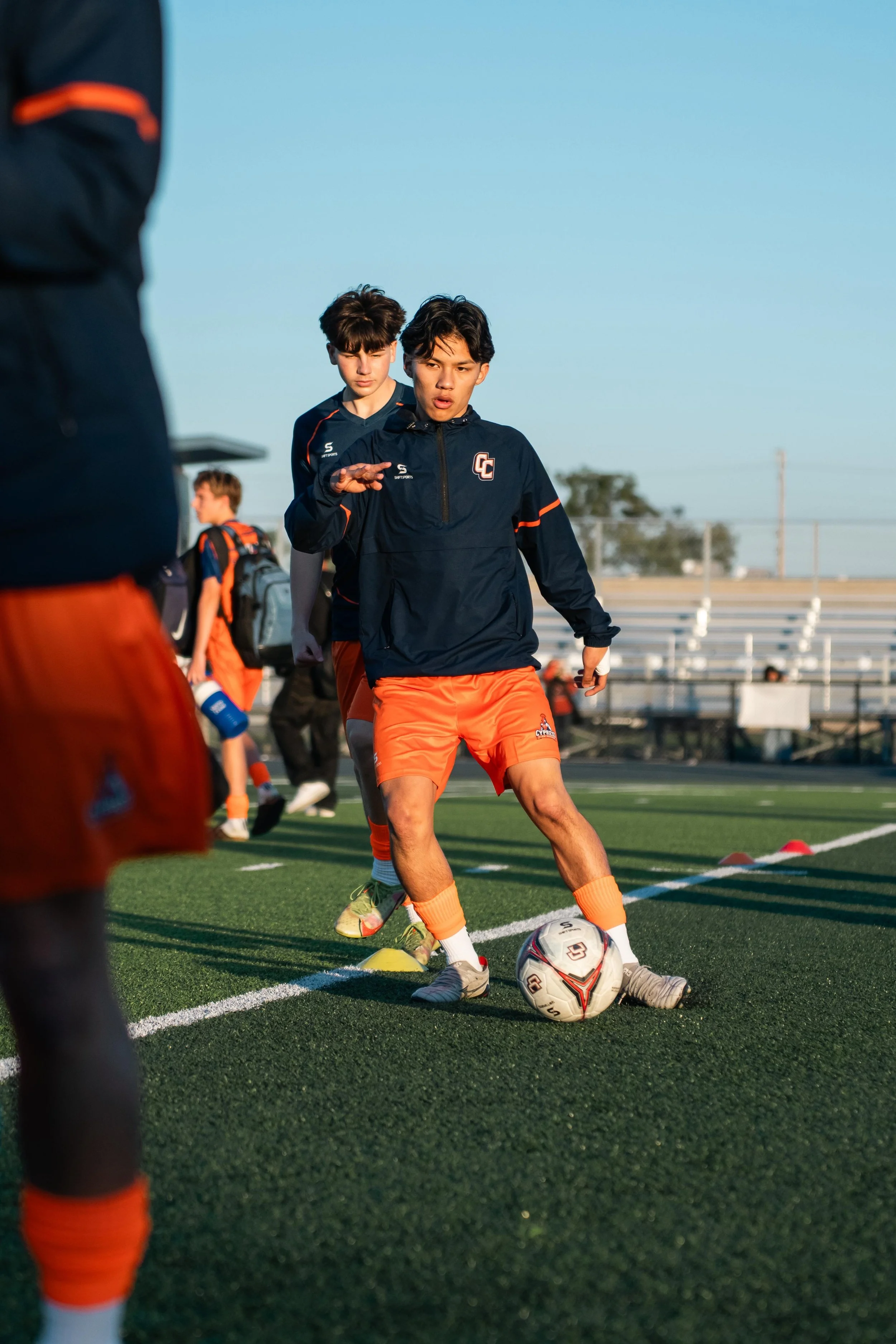 Soccer players in black training attire jogging on a sports field with cones, under a blue sky.