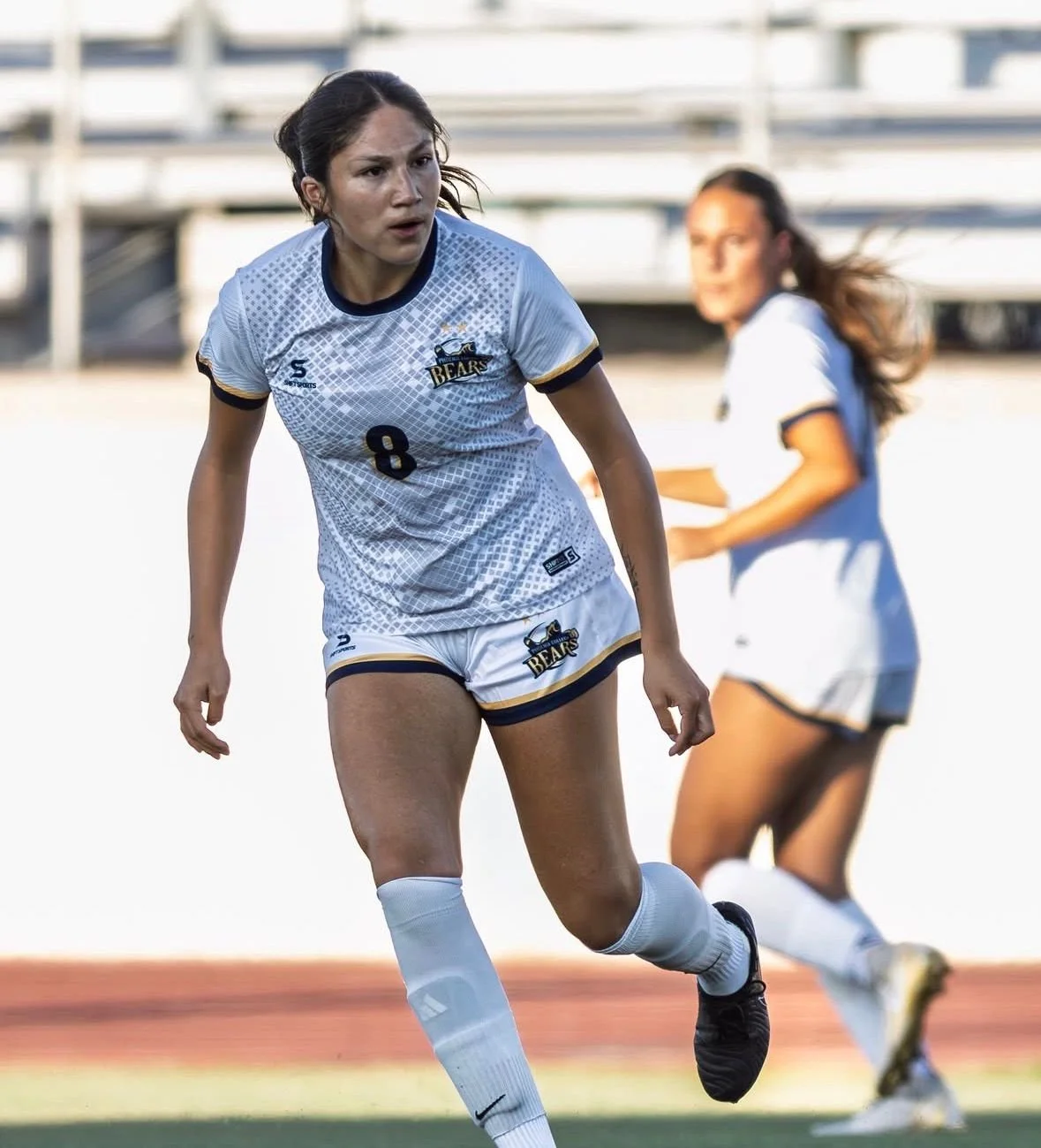 Soccer player in a white jersey kicking a soccer ball on a field.