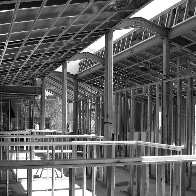 Black and white photo of a building under construction with exposed wooden framing and metal roofing.