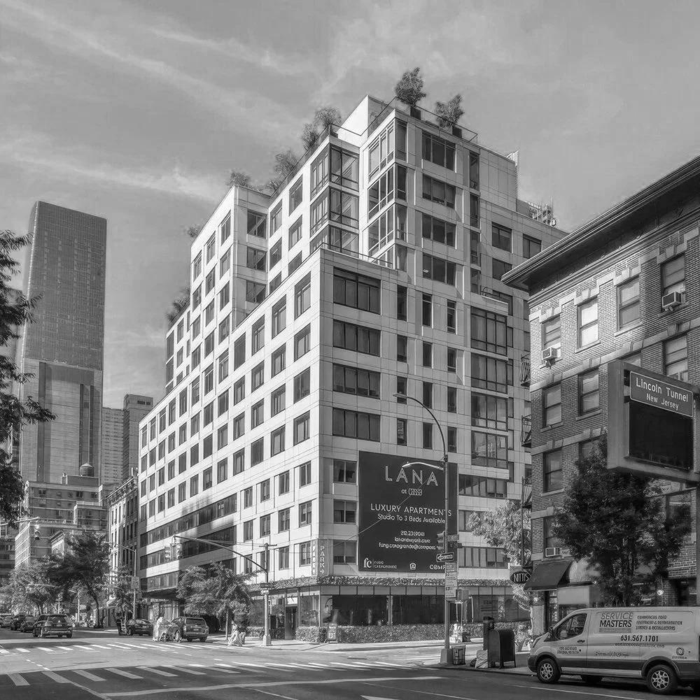 A modern multi-story building on a city street with cars parked along the curb and trees lining the sidewalk, black-and-white photo.