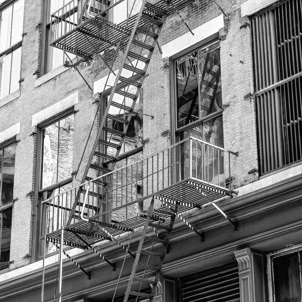 View of an exterior brick building with fire escape stairs and metal balconies, including windows and reflections.