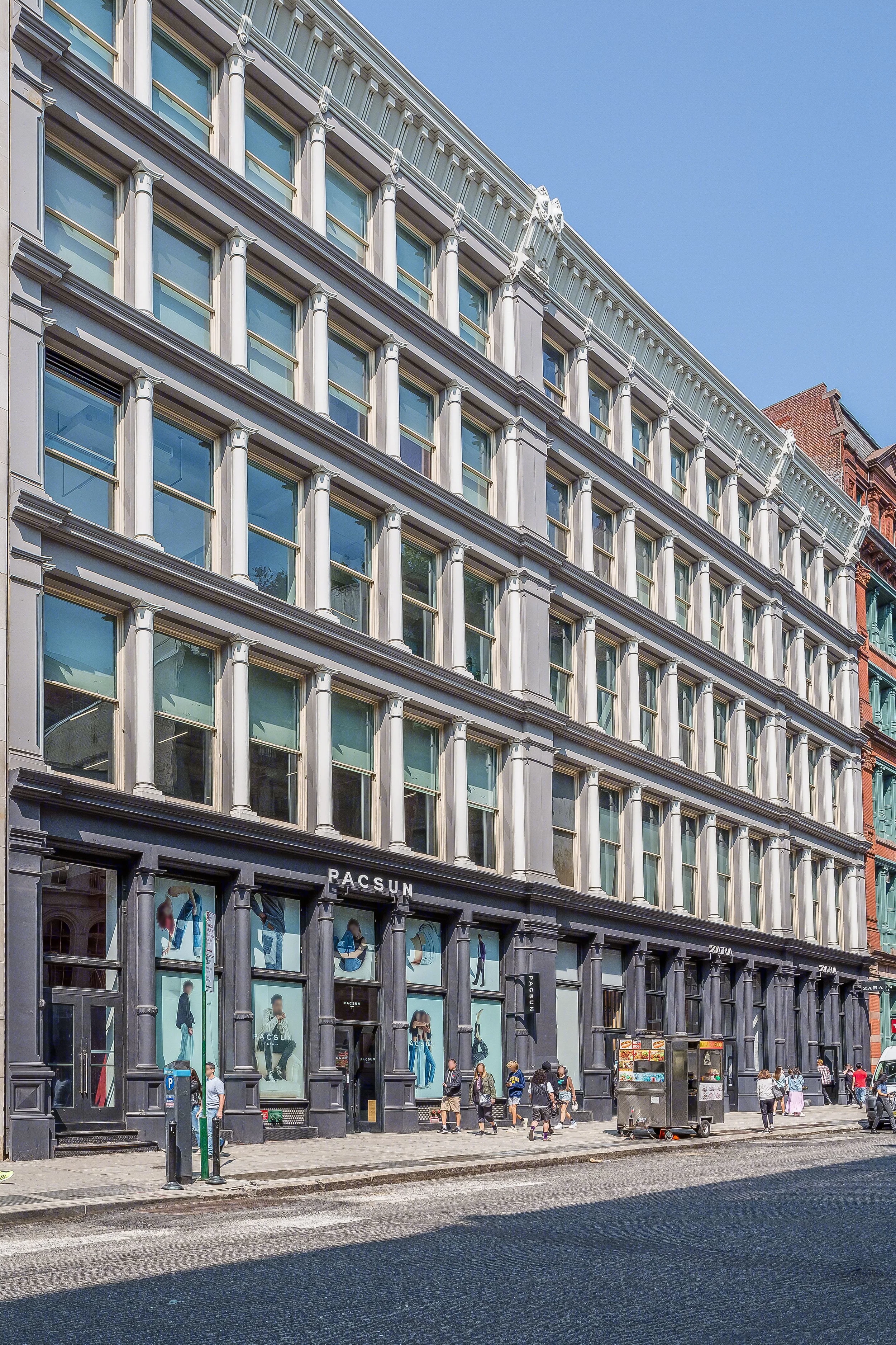 503-511 Broadway - A multi-story building with a black storefront at street level, showing mannequins and clothing displays, with the names 'PACSUN' and 'ZARA' above the windows, along a busy city sidewalk with pedestrians and a street vendor cart.
