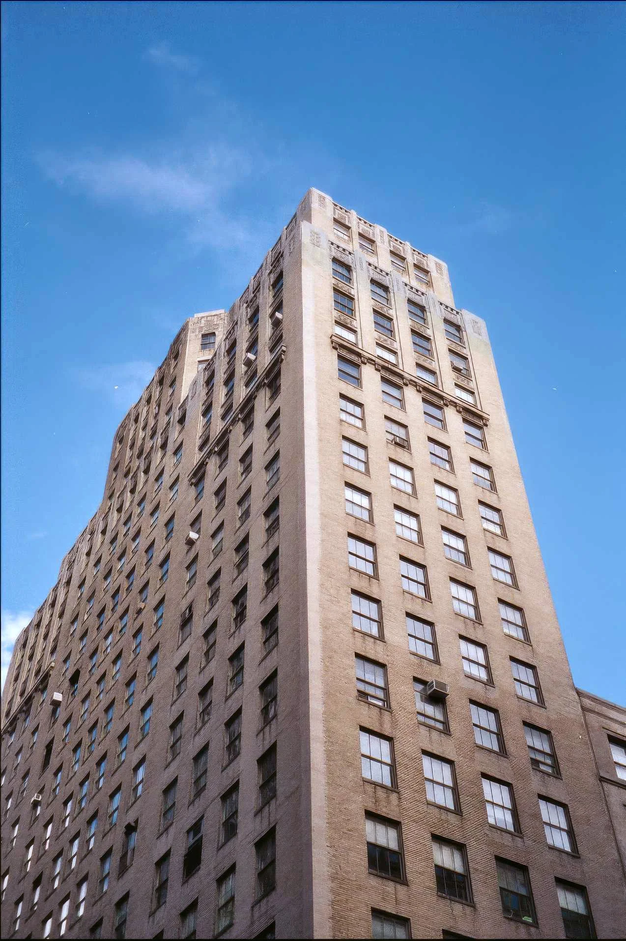 385 Park Ave. South - A tall, beige brick apartment building with many windows against a blue sky with a few clouds.